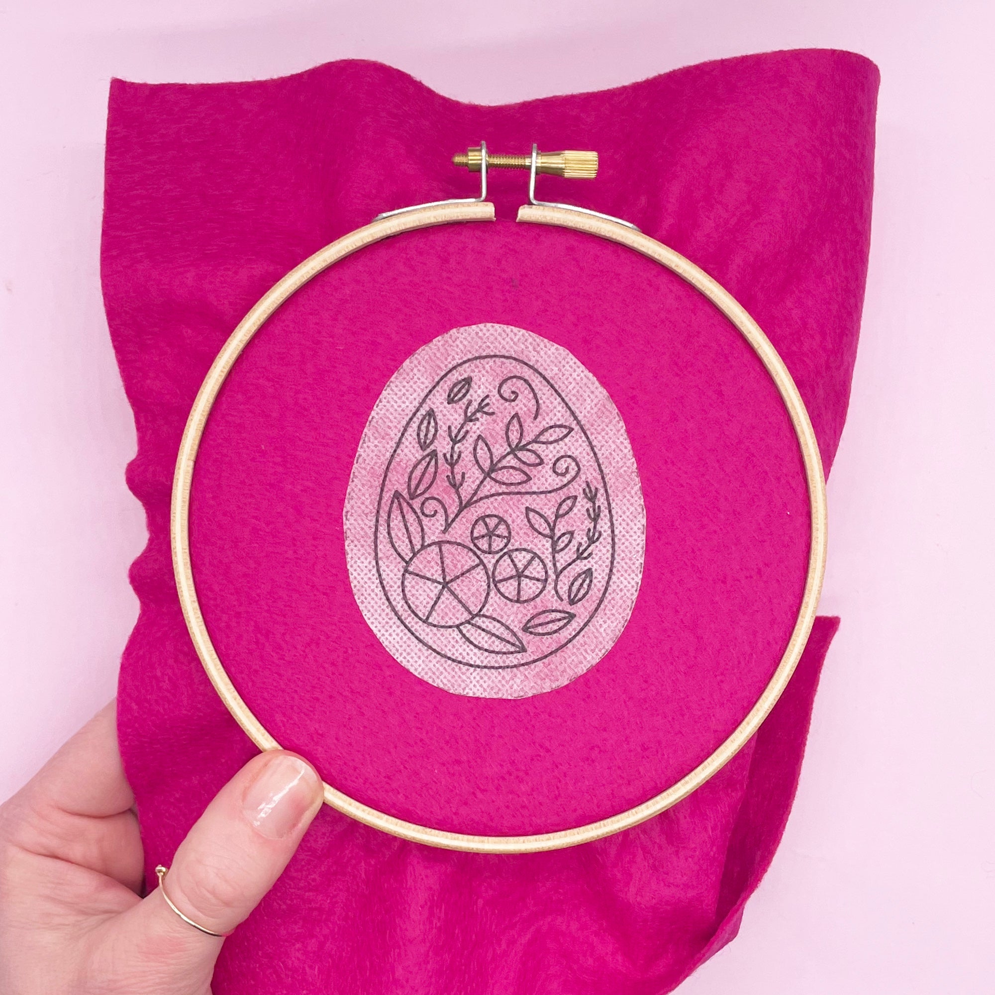 Easter egg embroidery pattern applied to bright pink fabric in a hoop. A dissolving stick and stitch embroidery design for Easter crafting.