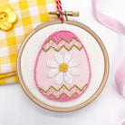 Stitched Easter embroidery design featuring a pink Easter egg with a daisy motif, framed in an embroidery hoop. A beautiful Easter craft idea for handmade decorations.