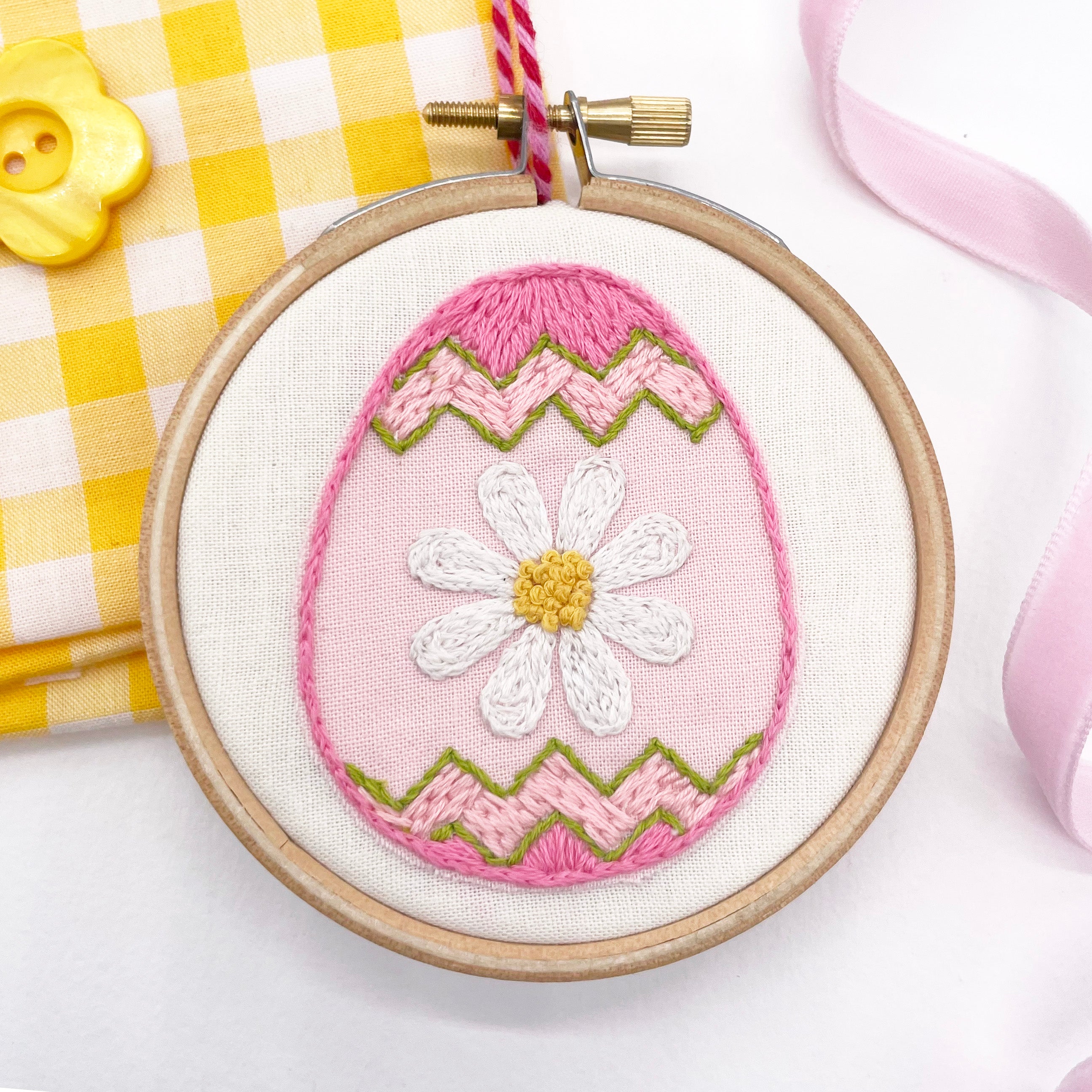 Stitched Easter embroidery design featuring a pink Easter egg with a daisy motif, framed in an embroidery hoop. A beautiful Easter craft idea for handmade decorations.