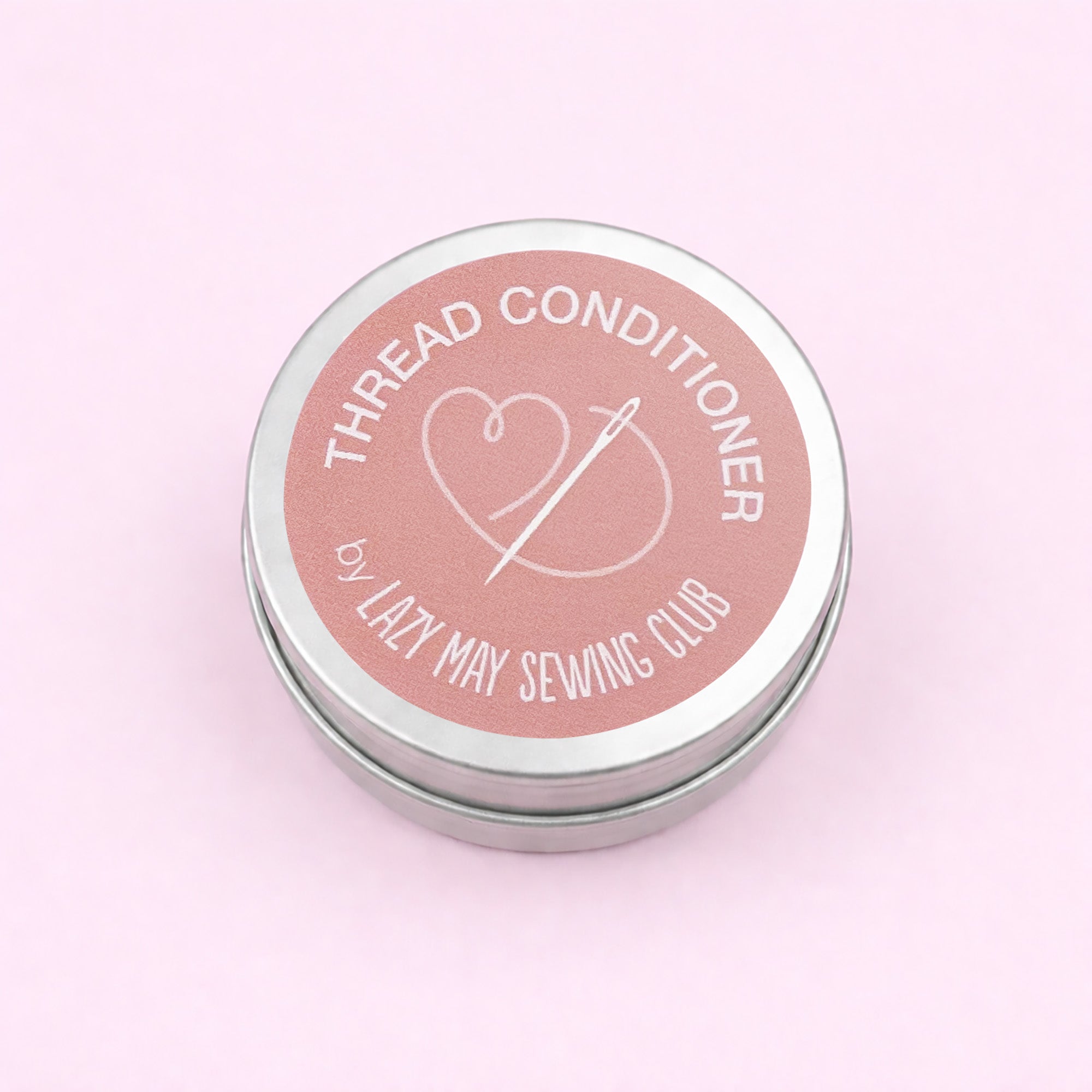 Thread conditioner container with pink lid and silver base on a light pink background