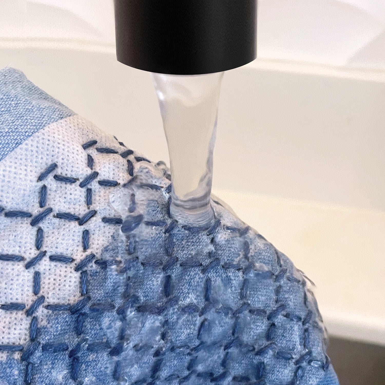 Water running over blue and white fabric featuring visible sashiko-style stitching and embroidery patterns