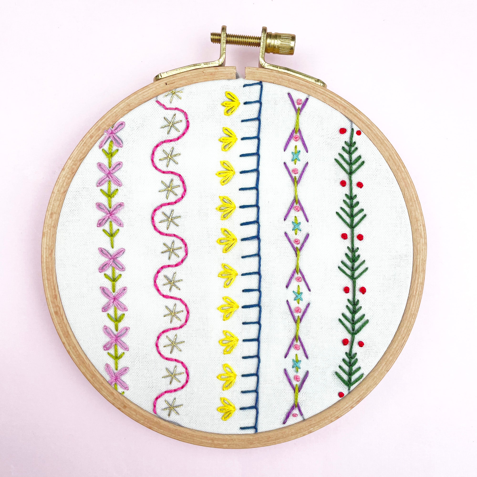 Iron-On Embroidery Patterns: 10 Embroidered Border Designs showing colorful stitched floral and geometric borders in embroidery hoop.