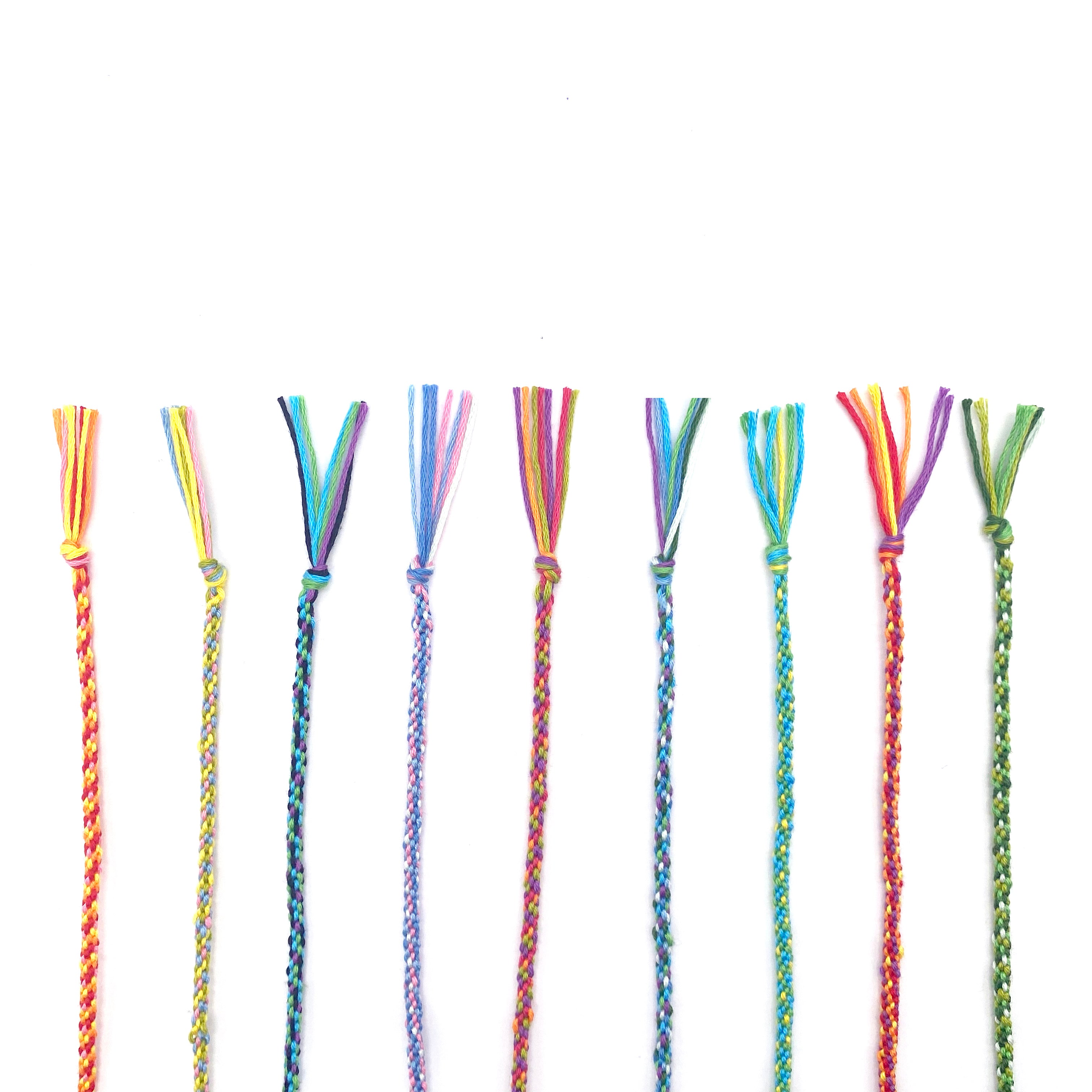 Six brightly coloured part-finished kumihimo braids laid flat in a row, each showing different colour combinations from the Lazy May beaded friendship bracelet kit.
