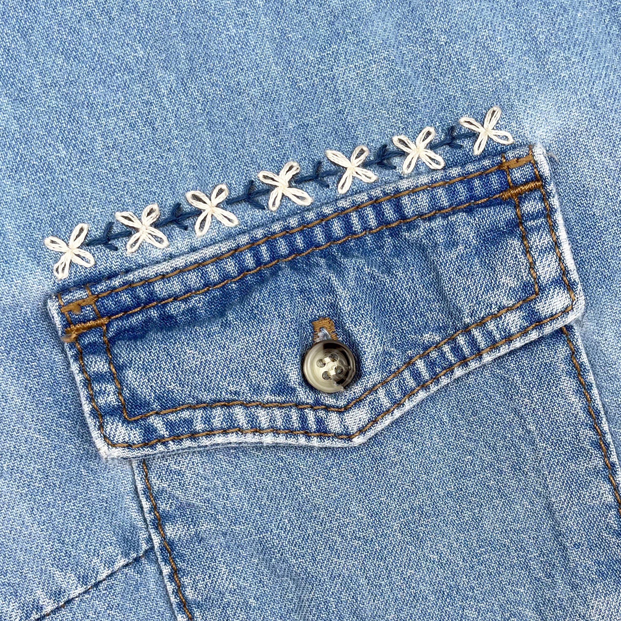 Iron-On Embroidery Patterns: 10 Embroidered Border Designs showing floral stitch detail on denim pocket edge with white thread.