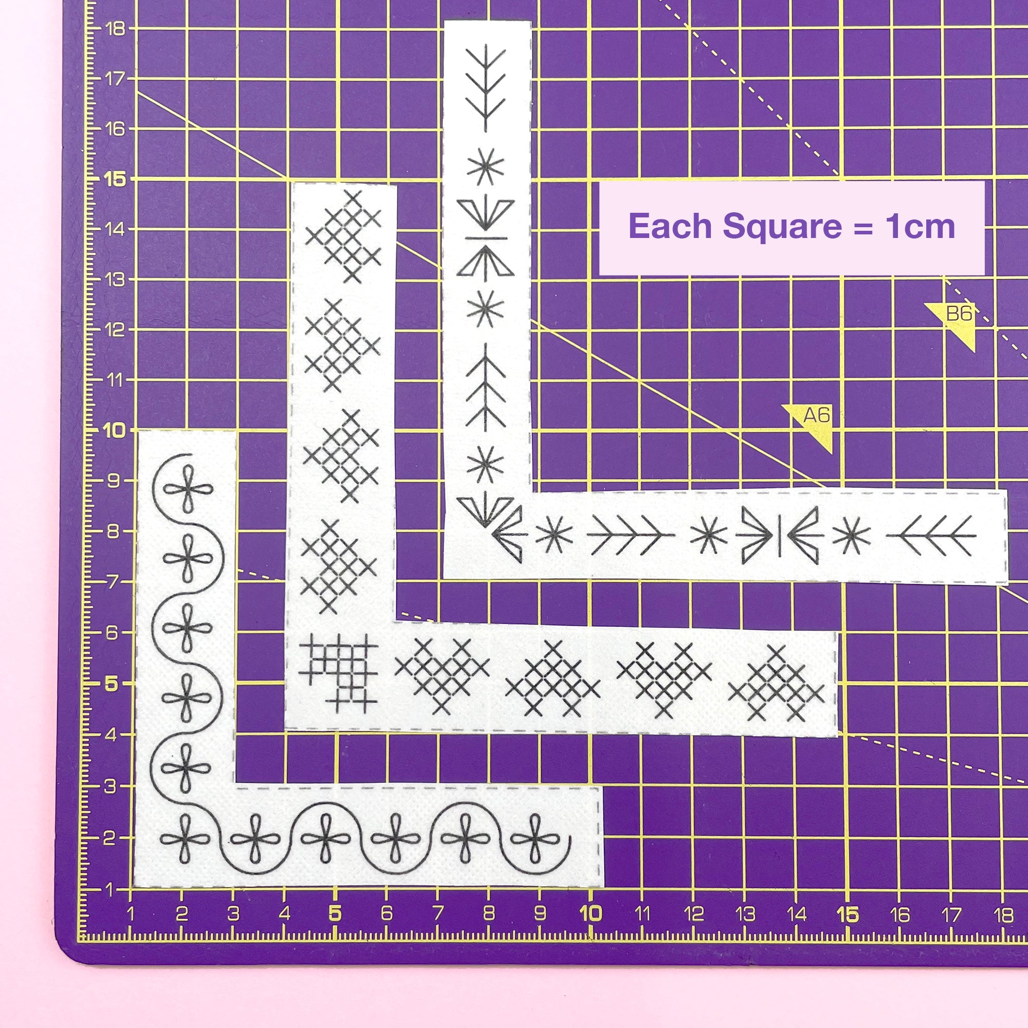 Corner embroidery patterns laid out on a purple cutting mat showing scale, with a 1cm grid.