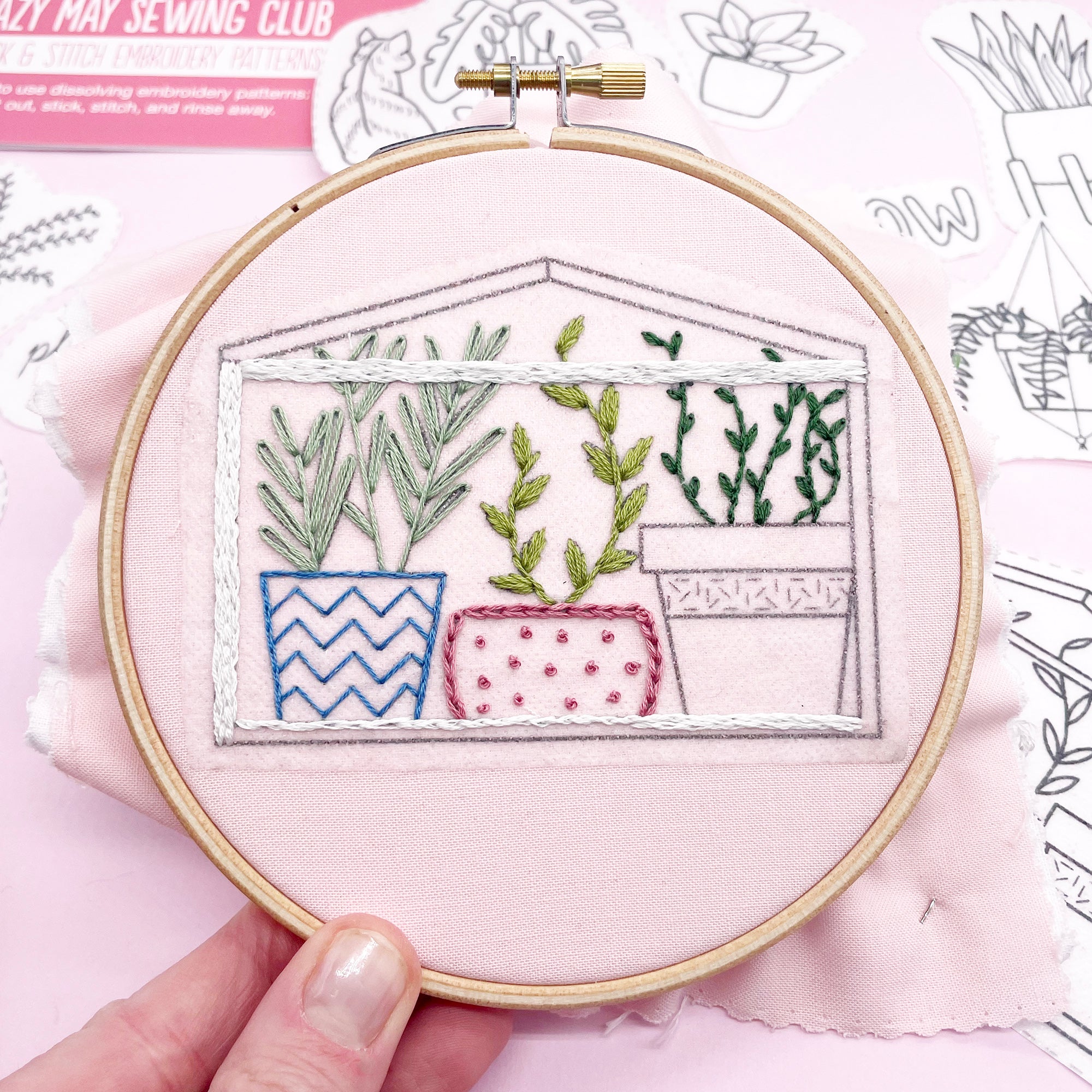 A finished embroidery of a greenhouse with potted plants, using stick and stitch modern embroidery patterns.