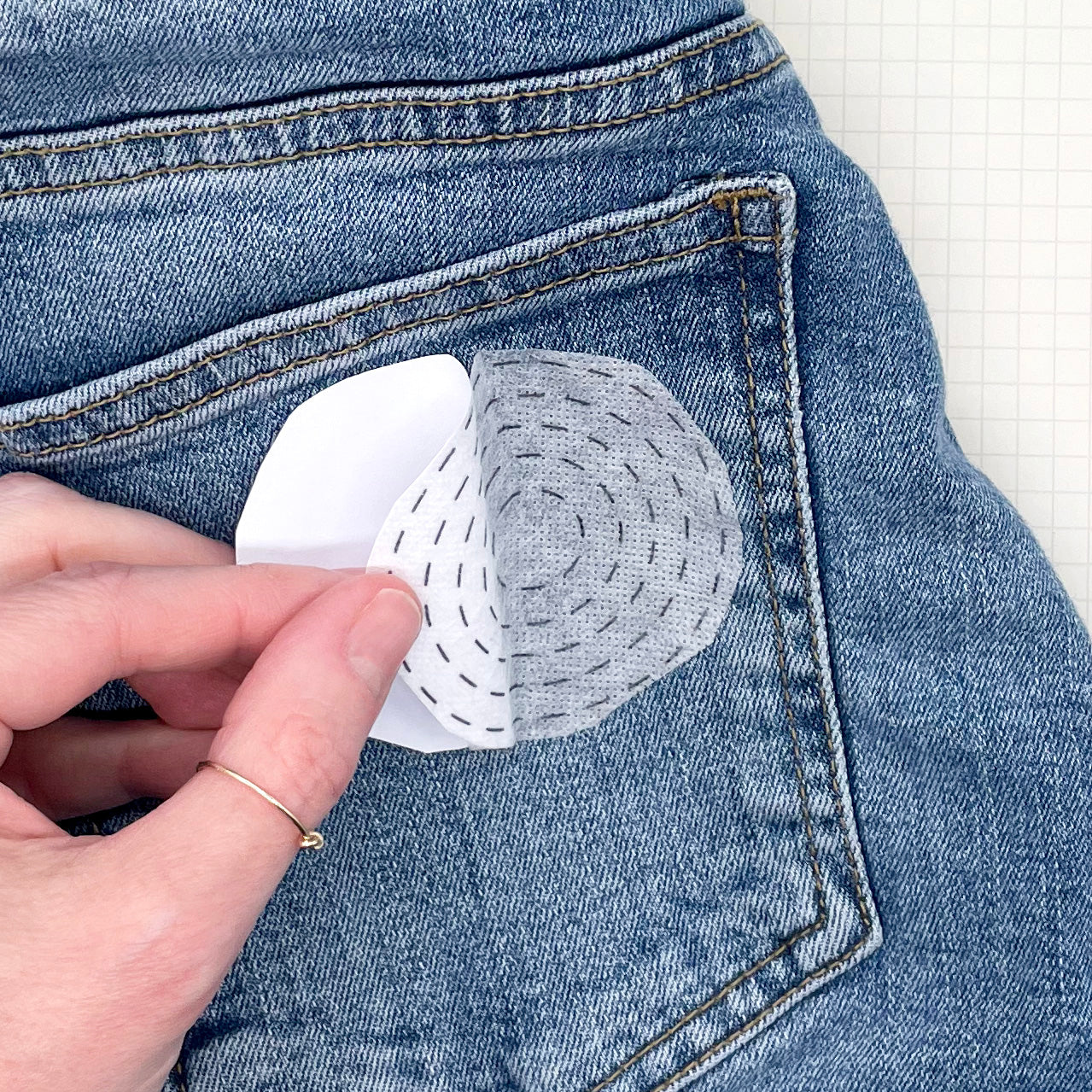 Visible Mending Kit: Sashiko Inspired Stick and Stitch Patterns showing hand lifting fabric patch on denim pocket with embroidery.