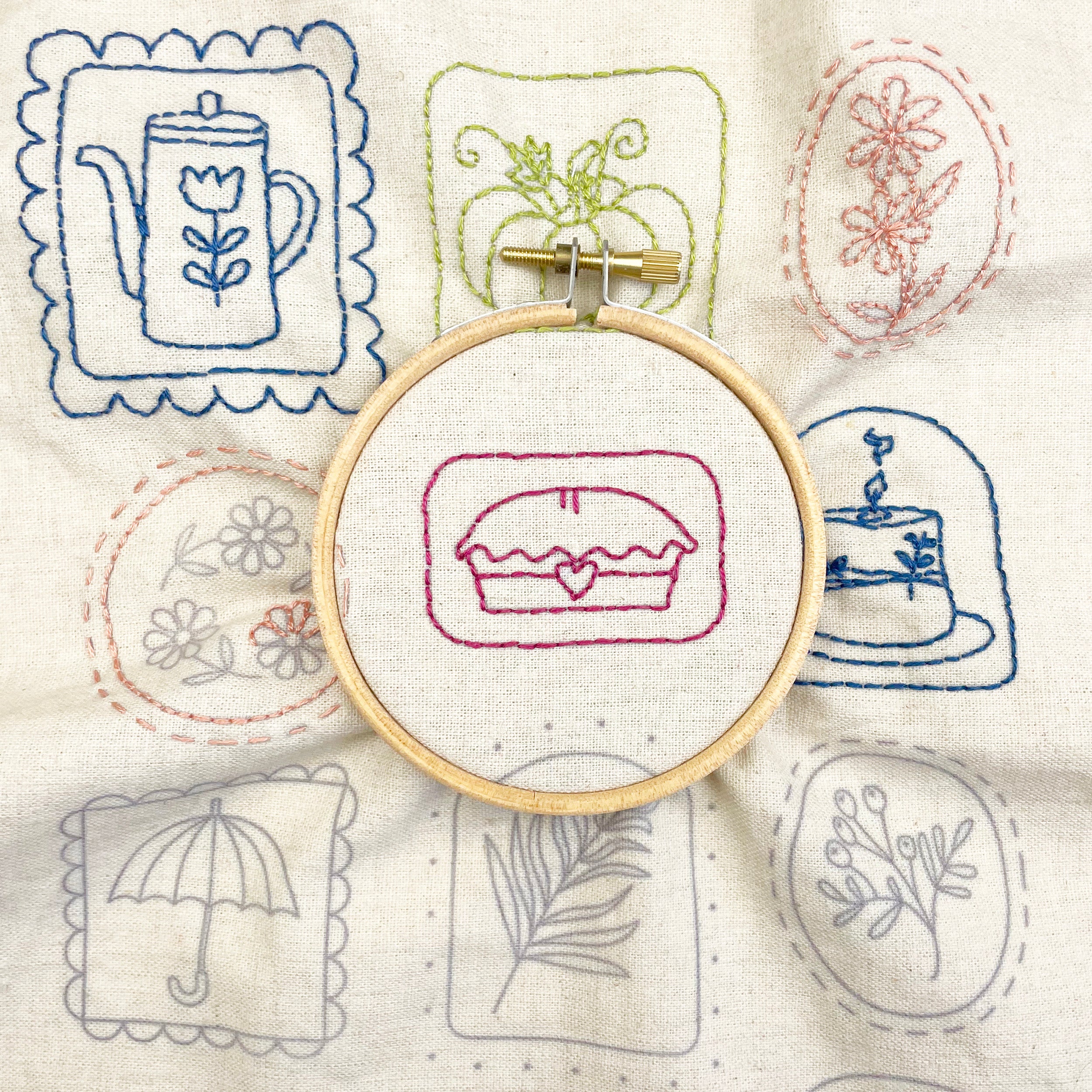 Embroidery hoop with a embroidered design on a fabric background with other embroidered patterns.