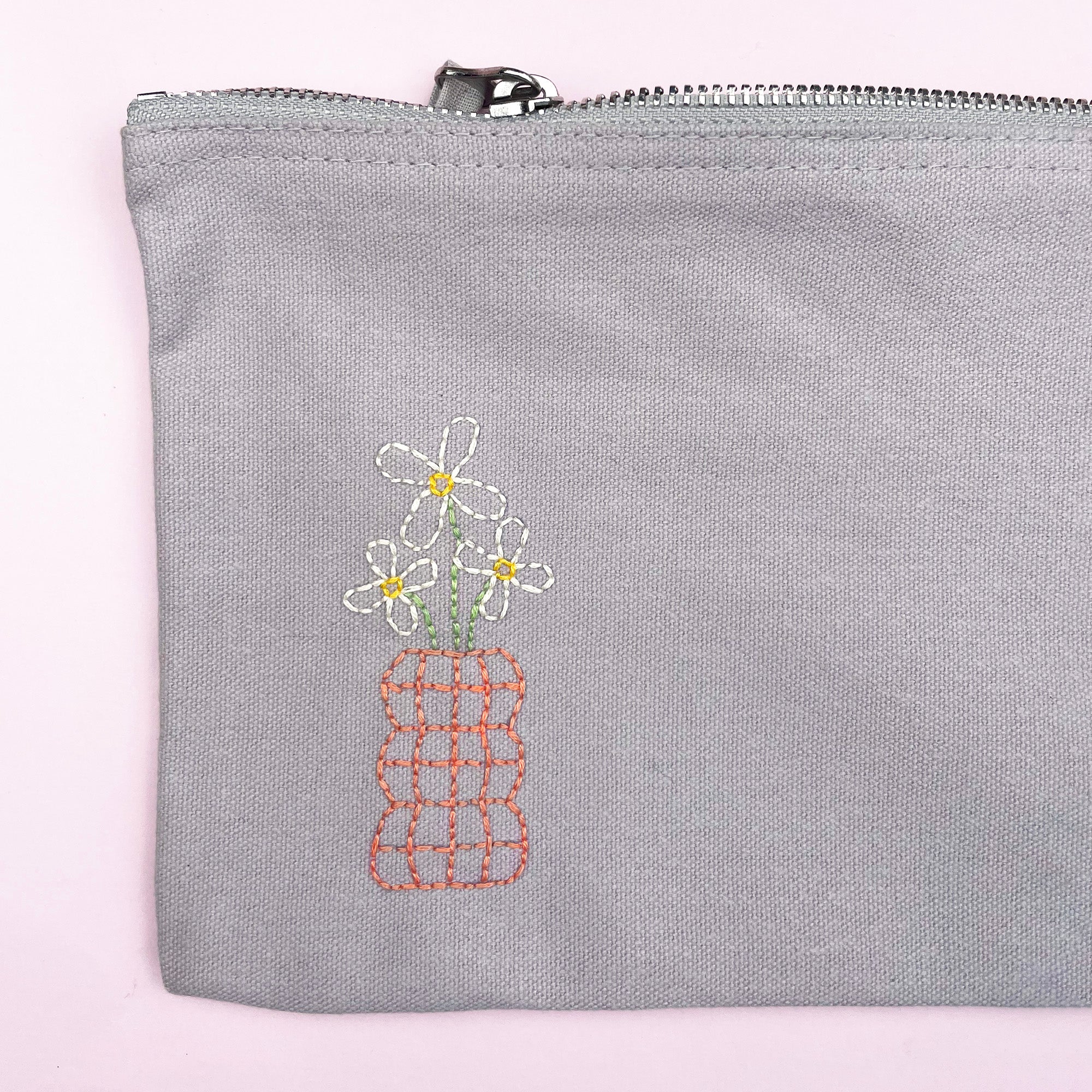 Gray pouch with embroidered flowers on a light pink background