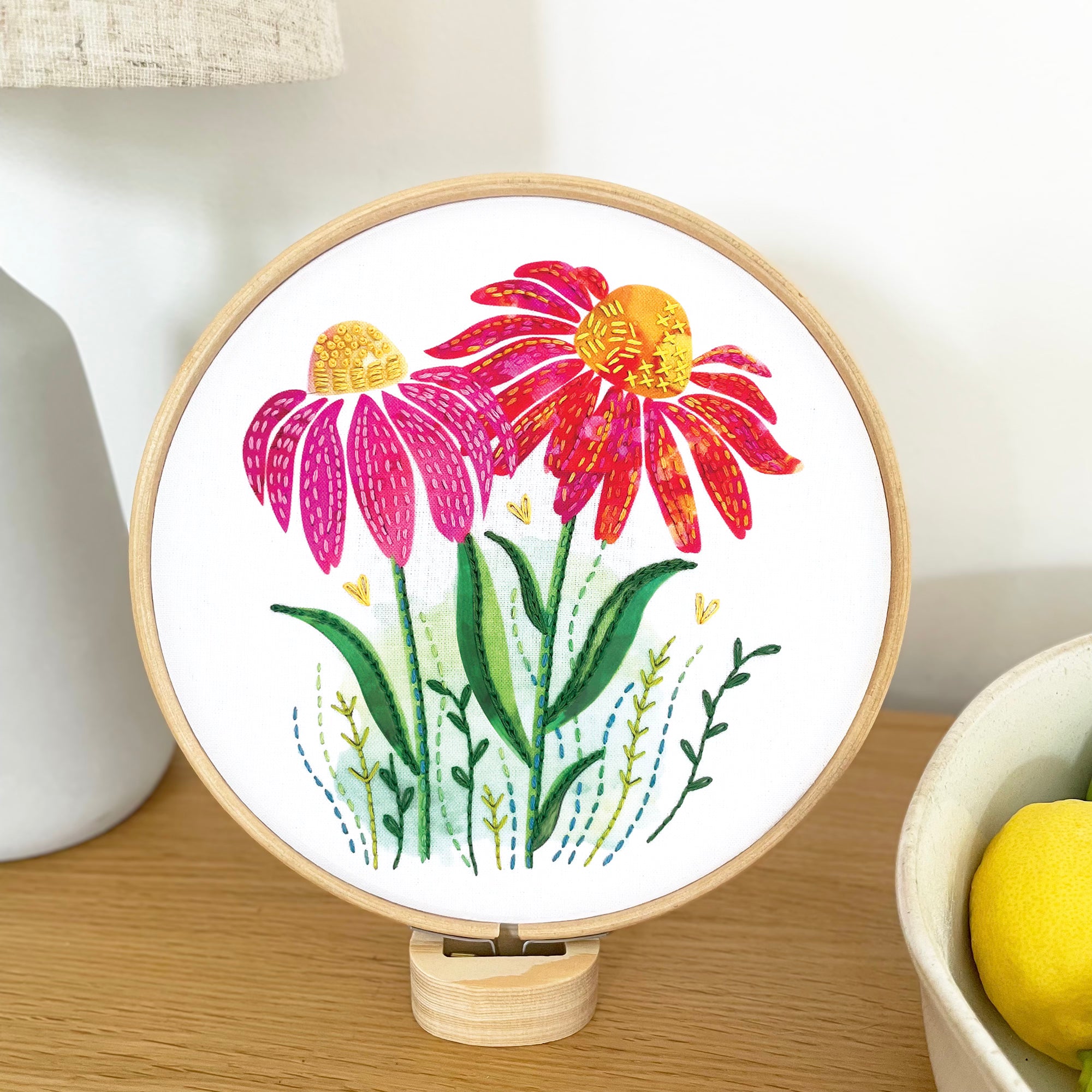 floral embroidery hoop with pink and yellow cone flowers displayed on a wooden hoop stand