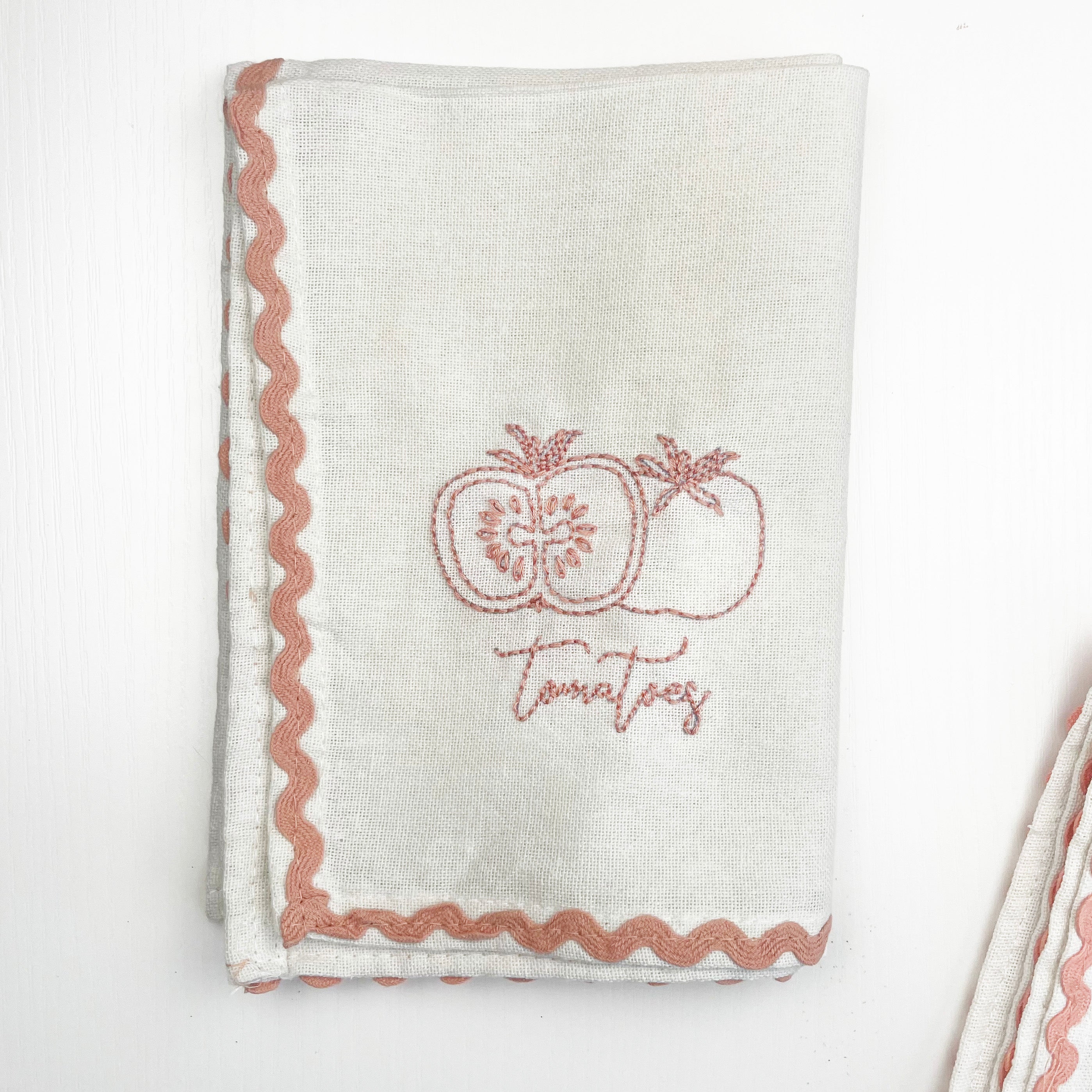White towel with pink embroidered apples and 'Tomatoes' text on a white background