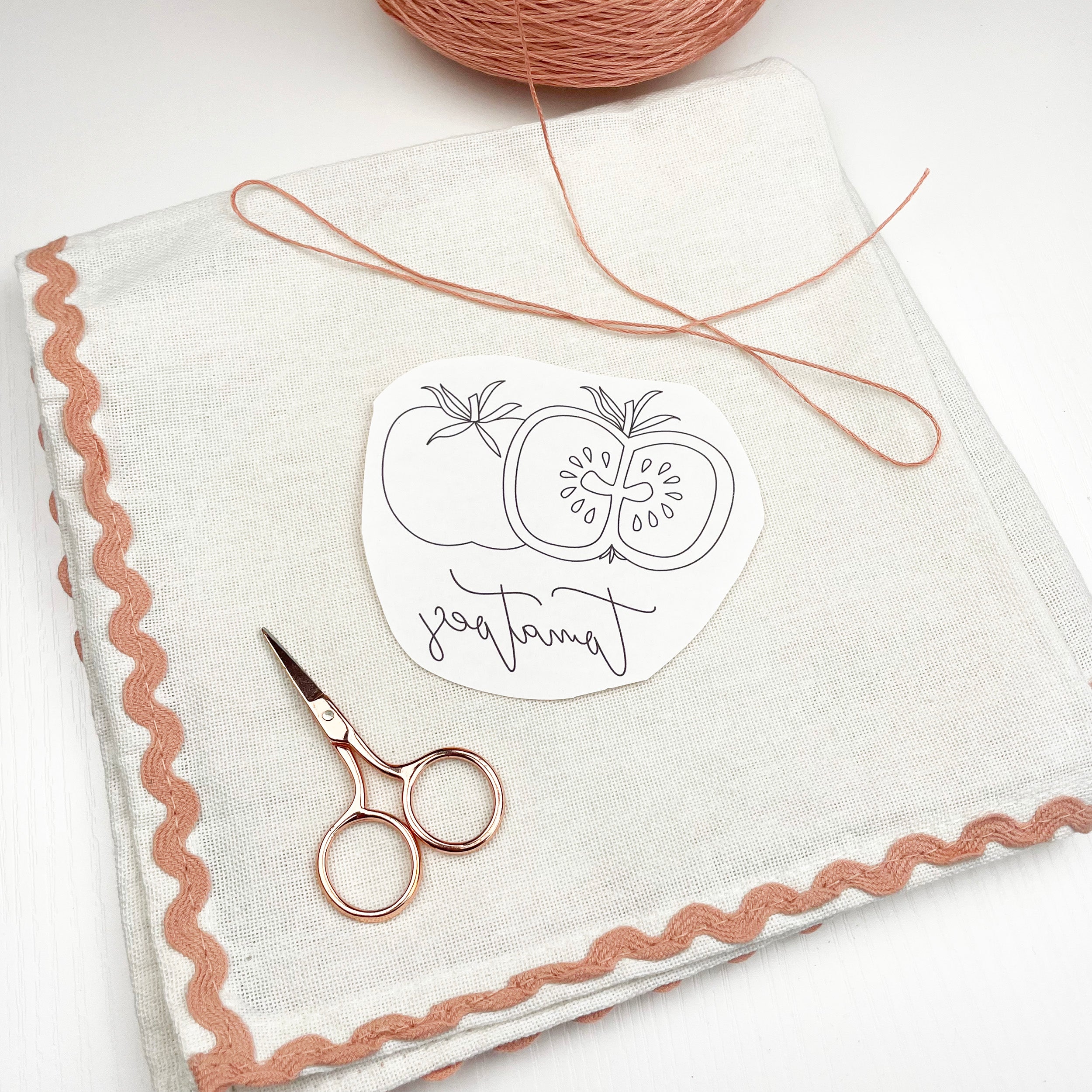 Fabric with embroidered design, scissors, and yarn on a white background