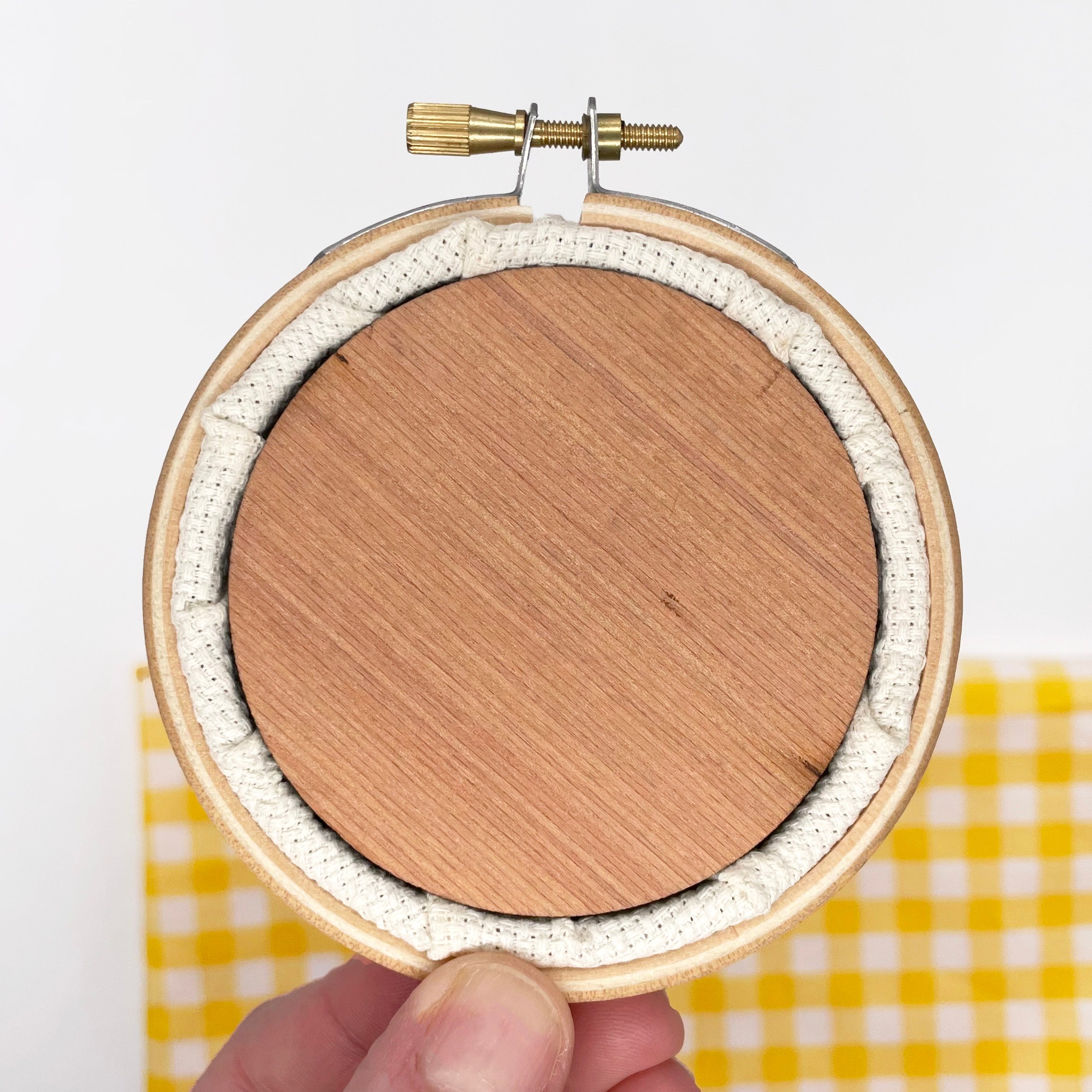 Hand holding wooden embroidery hoop with fabric stretched inside, for Tiny Garden: Cross Stitch Kit project.