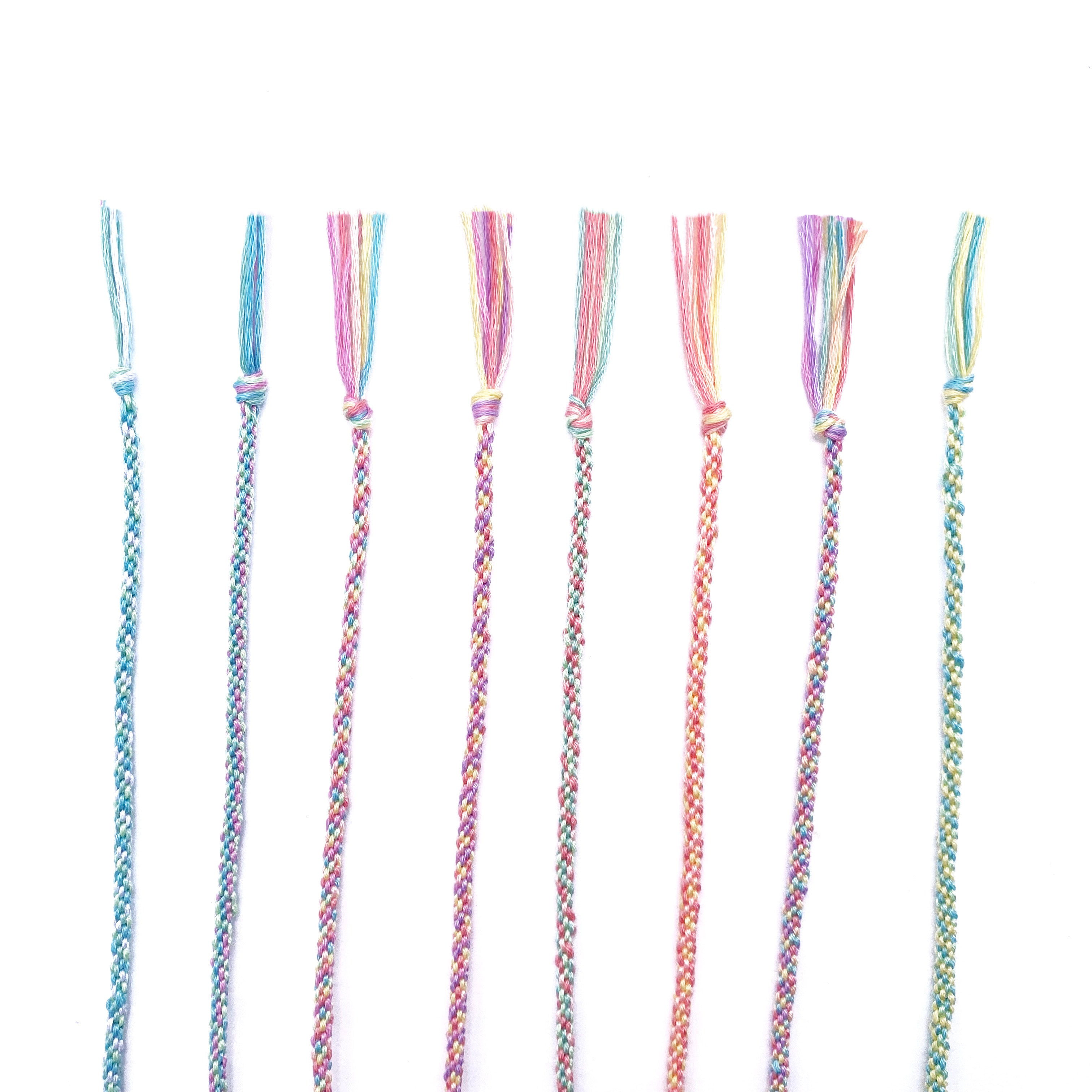 eight handmade kumihimo bracelets in pastel colours, partially woven using the Lazy May friendship bracelet kit.