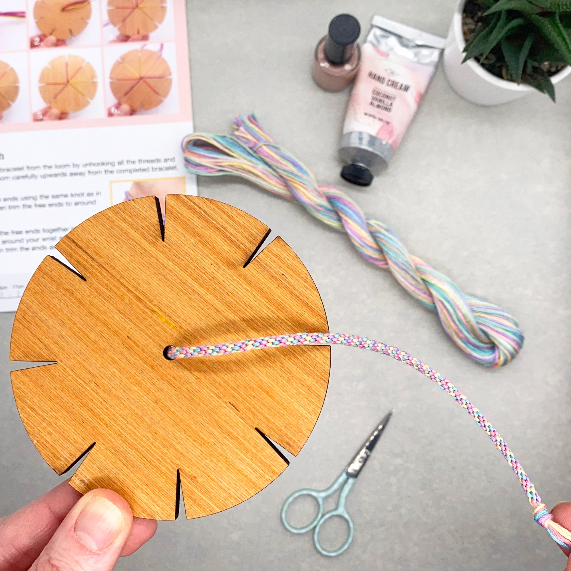Close-up of kumihimo bracelet being woven on a wooden loom from the woven bracelet kit – shows pastel threads and simple setup.