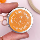 Thread conditioner tin held by a hand with sewing tools in the background