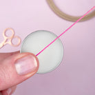 Hand holding a spool of pink thread with scissors on a light purple background