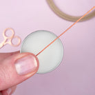 Close-up of a hand holding a spool of thread with scissors on a light pink background
