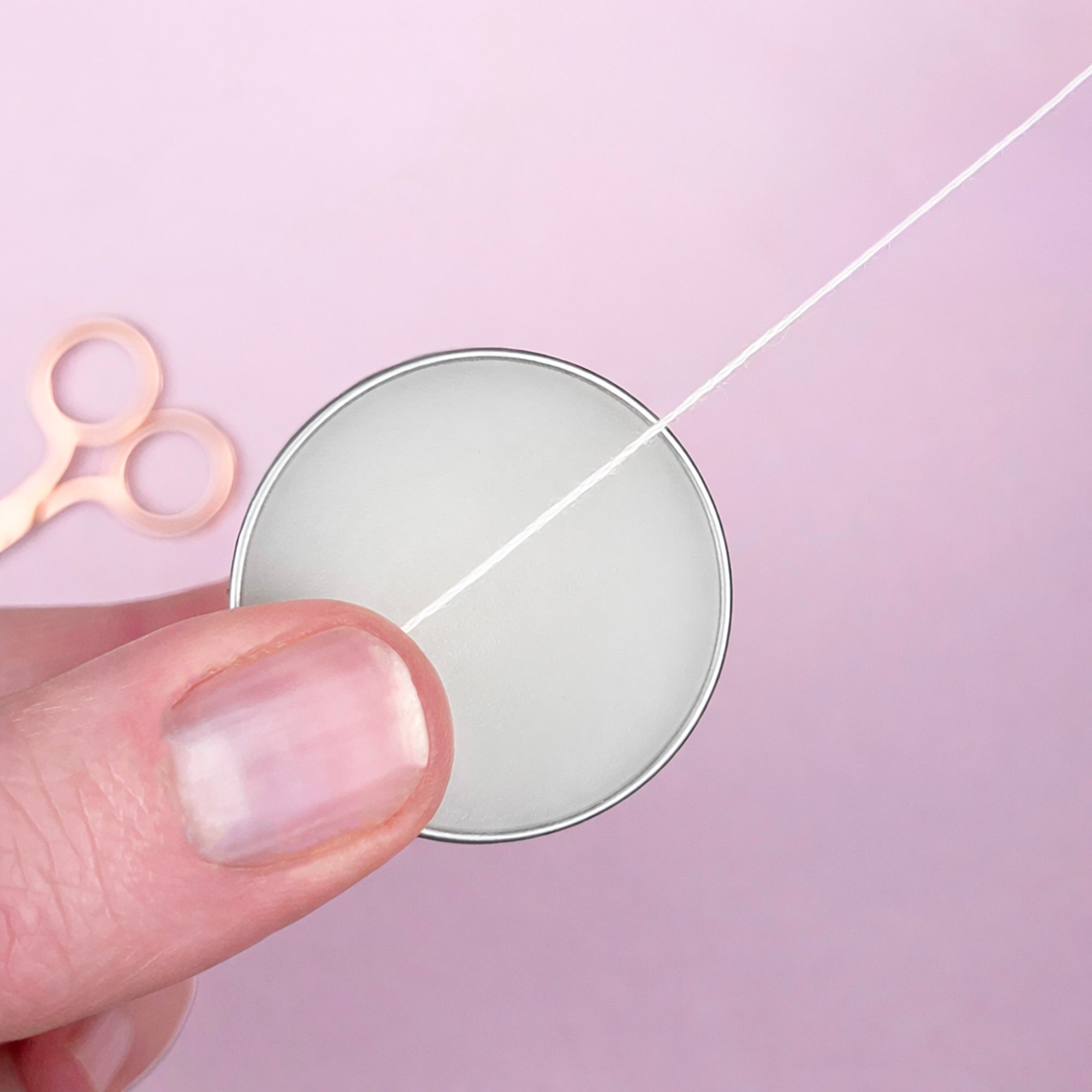 Hand holding a spool of thread with scissors on a pink background