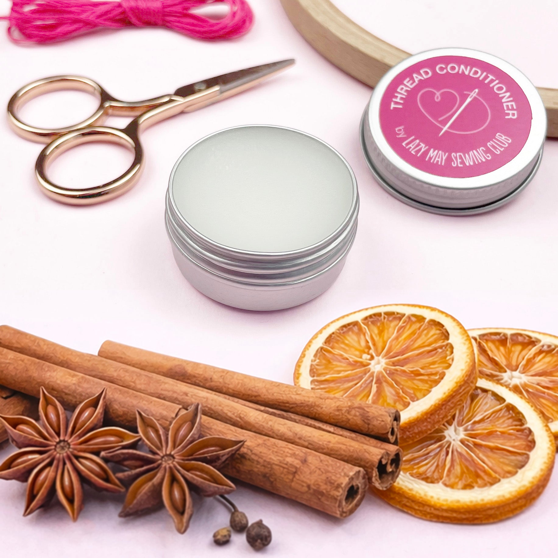 Thread conditioner container, cinnamon sticks, star anise, dried oranges, and scissors on a white background.