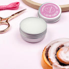 Silver containers with pink lids, scissors, and a cinnamon roll on a light pink background