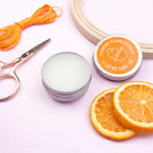 Thread conditioner with orange slices and sewing tools on a light pink background