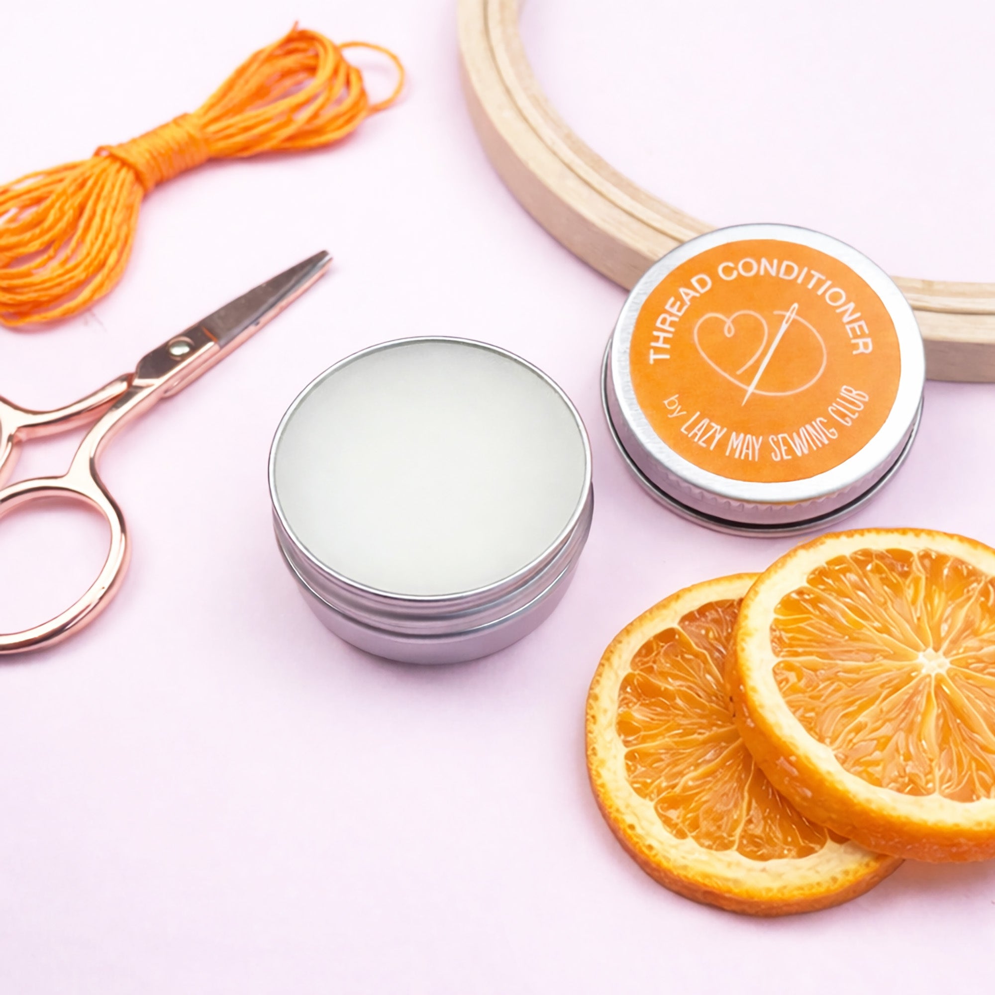 Thread conditioner with orange slices and sewing tools on a light pink background