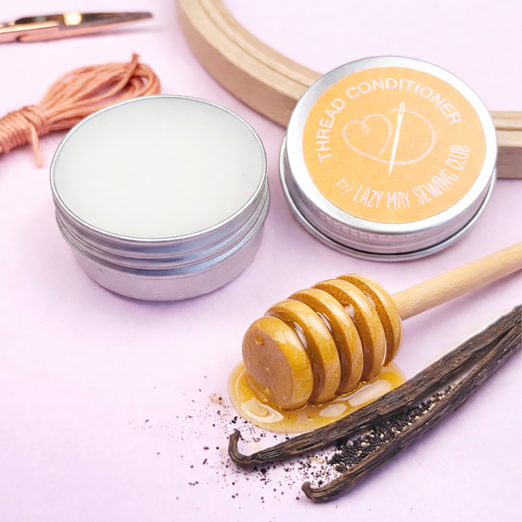 Two tins labeled 'Thread Conditioner' with a honeycomb and vanilla bean on a pink background.