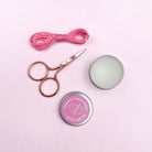 Pair of scissors, pink thread, and two tins on a pink background