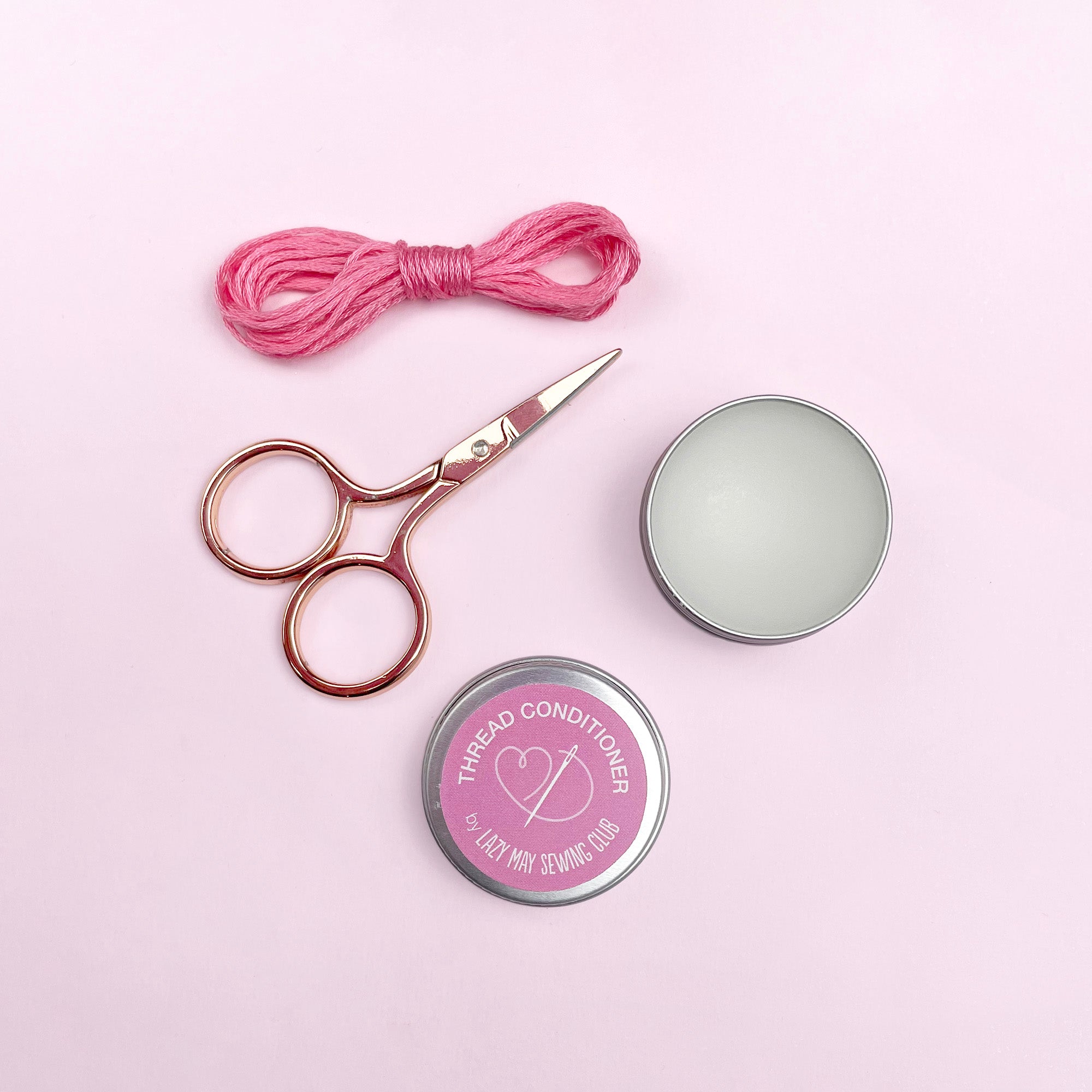 Pair of scissors, pink thread, and two tins on a pink background