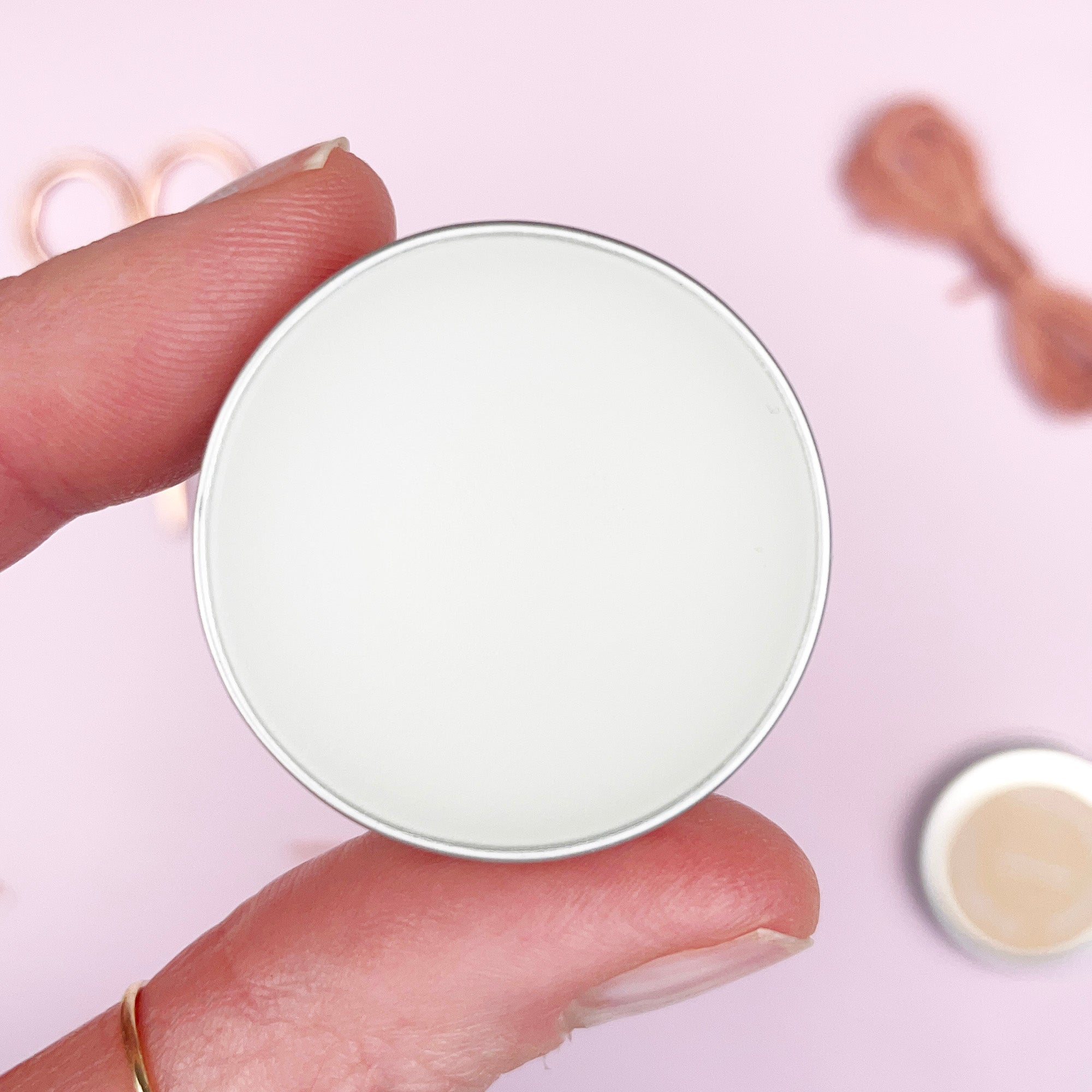 Round white object held between fingers on a light pink background