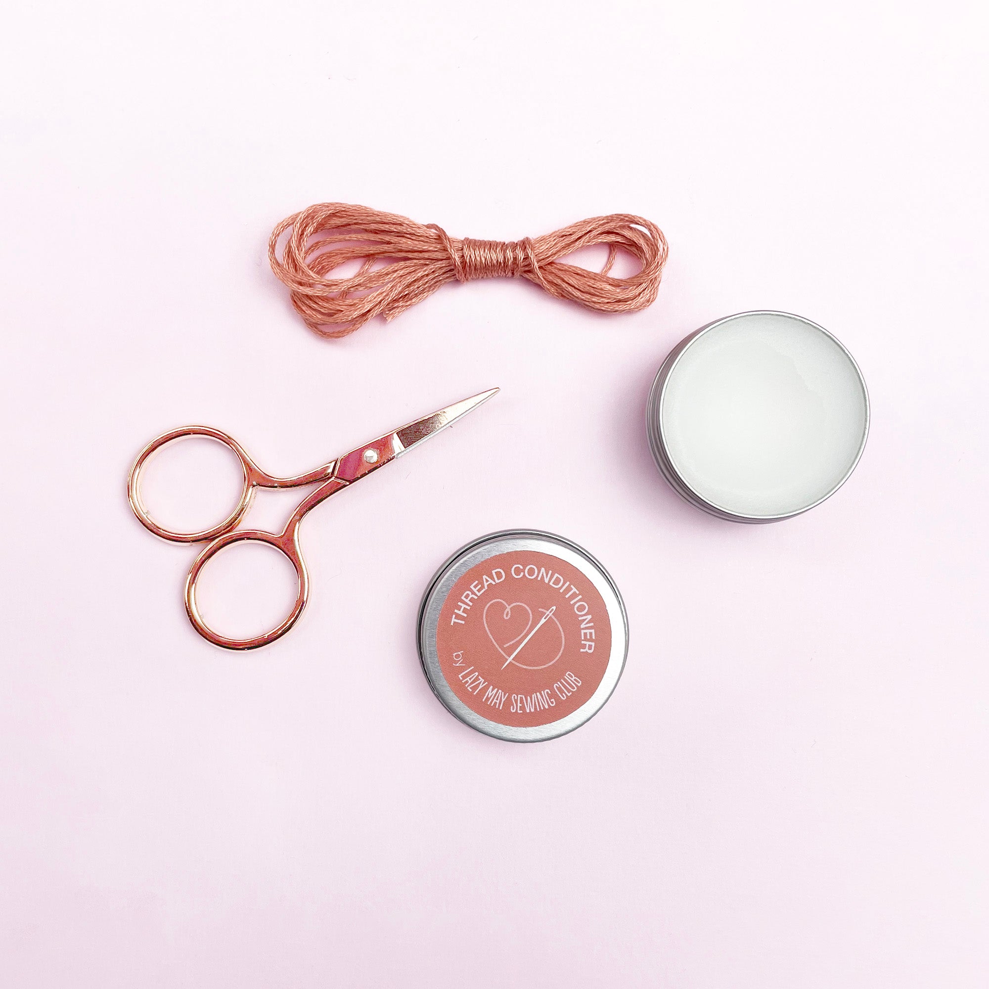 Thread conditioner, scissors, and thread on a light pink background