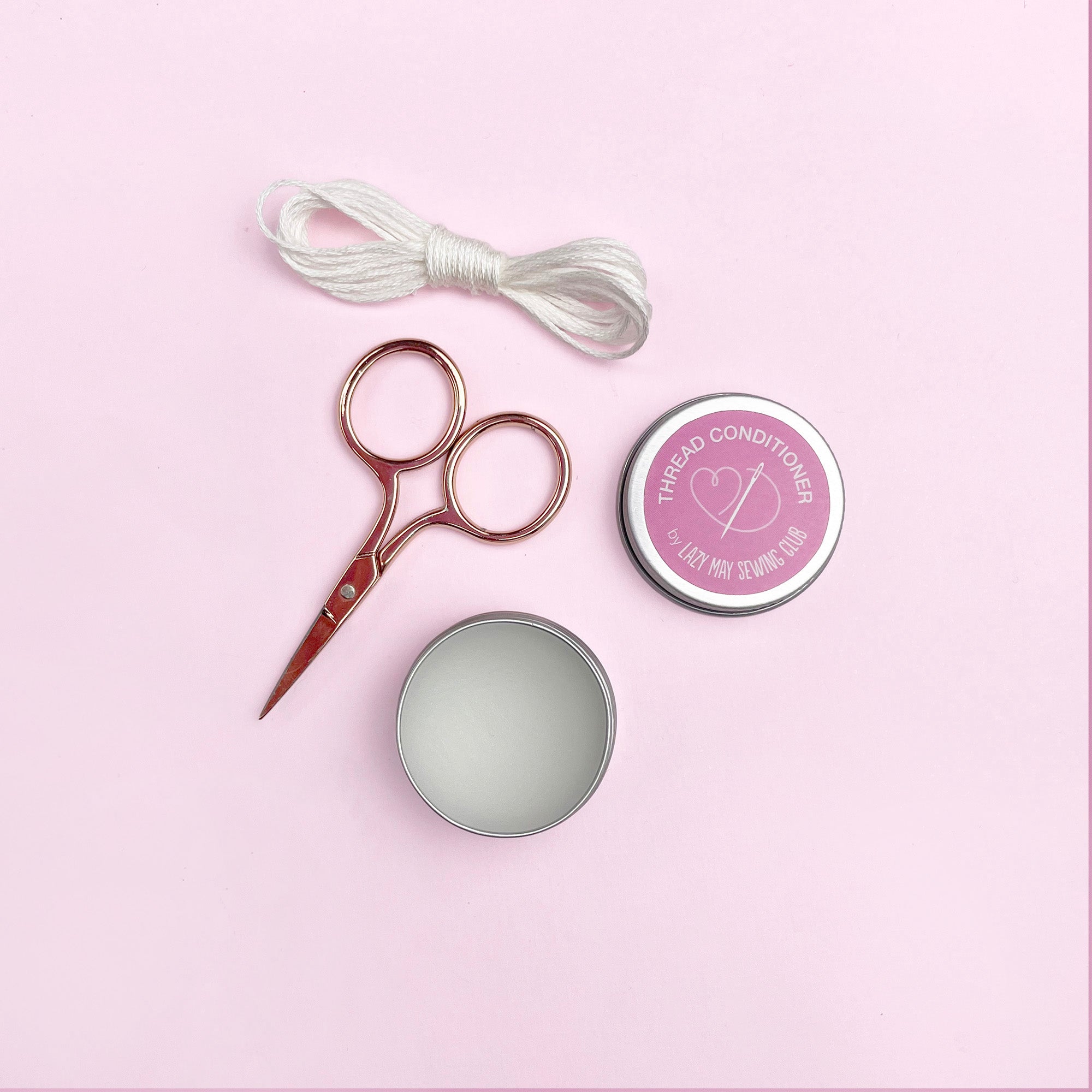 Scissors and thread on a pink background
