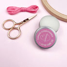 Thread conditioner tin with pink label, scissors, and pink thread on a light pink background