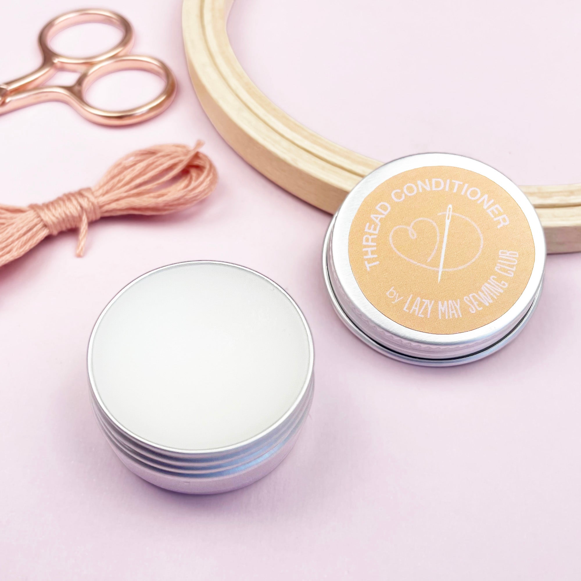 Thread conditioner container with a lid, scissors, and thread on a pink background