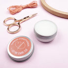 Thread conditioner container with sewing tools on a pink background