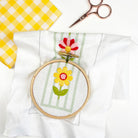Embroidery hoop with floral design on a white fabric background. In-progress stitching of a flower using a 3" embroidery hoop. Easy embroidery bookmark project using pre-printed fabric and thread.