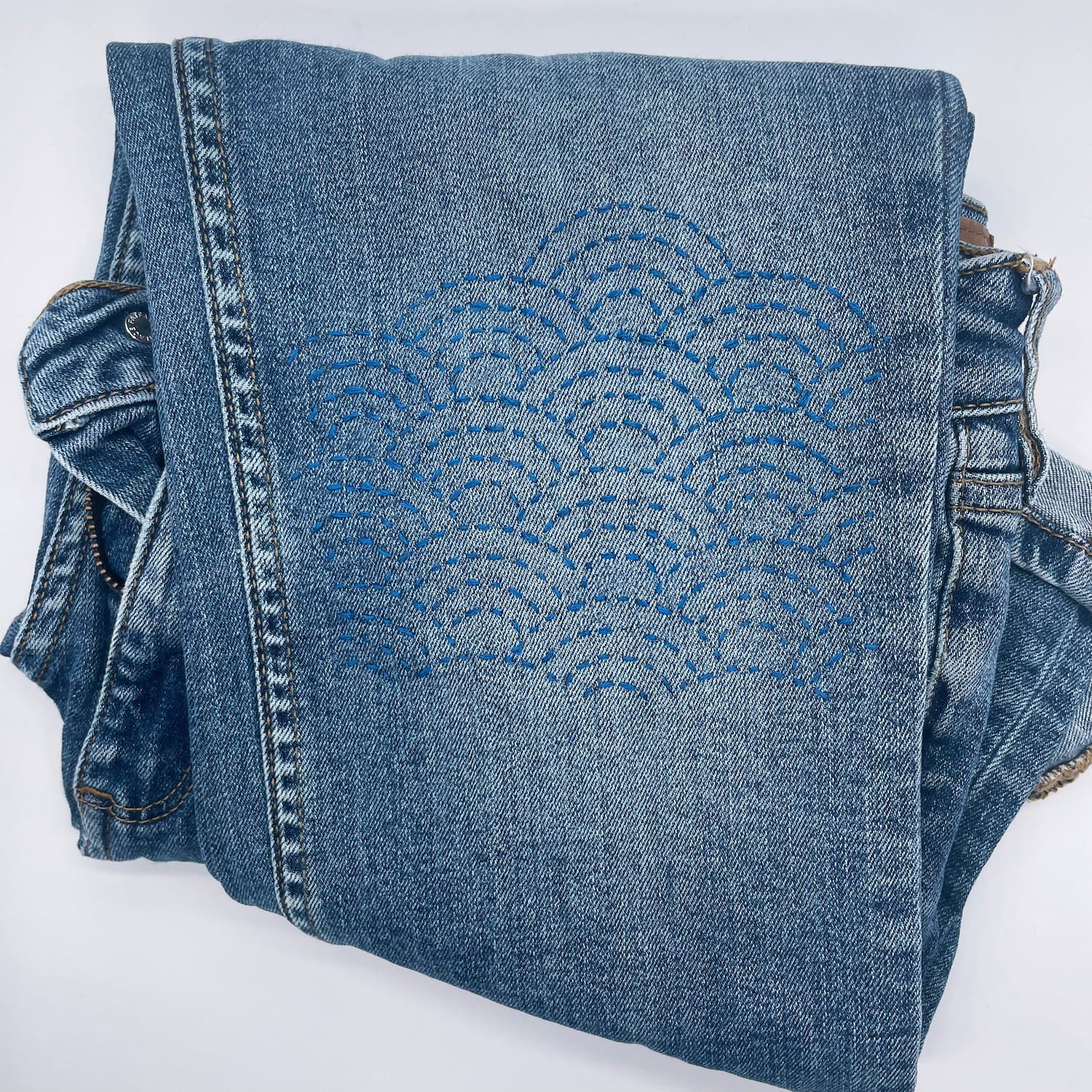 Visible Mending Kit: Sashiko Inspired Stick and Stitch Patterns with blue embroidery on folded denim jeans.