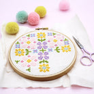 A partially stitched floral cross-stitch piece in progress, held within an embroidery hoop. The image highlights the neat stitches and the variety of colorful threads used, demonstrating the crafting process.