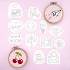 A selection of doodle-style iron-on embroidery patterns featuring hearts, cherries, a roller skate, and a sun. A completed embroidered paper plane design is displayed in a hoop, ideal for Easter crafts and DIY embroidery projects.
