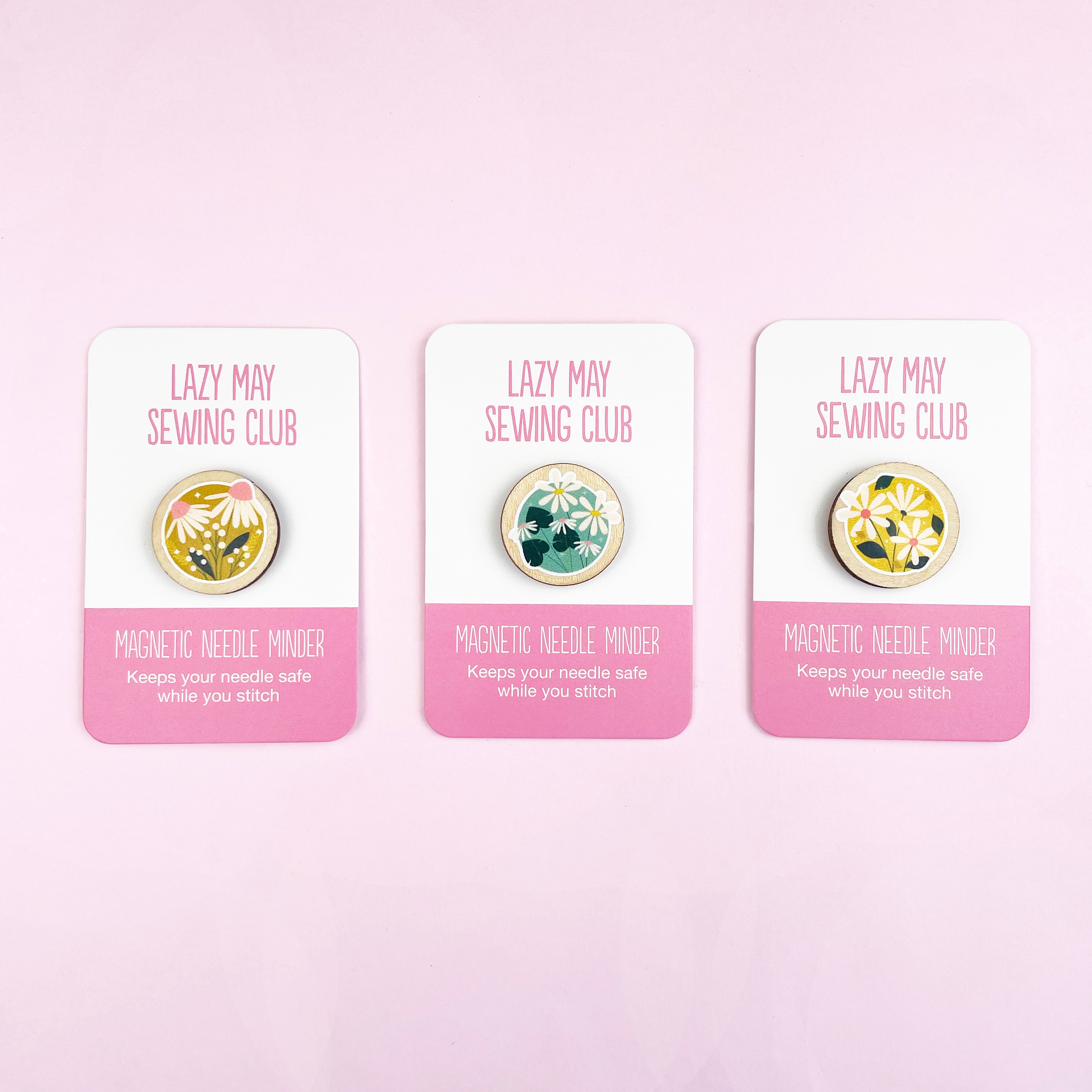 Three Lazy May Sewing Club floral wooden magnetic needle minders on their packaging with a pink background.