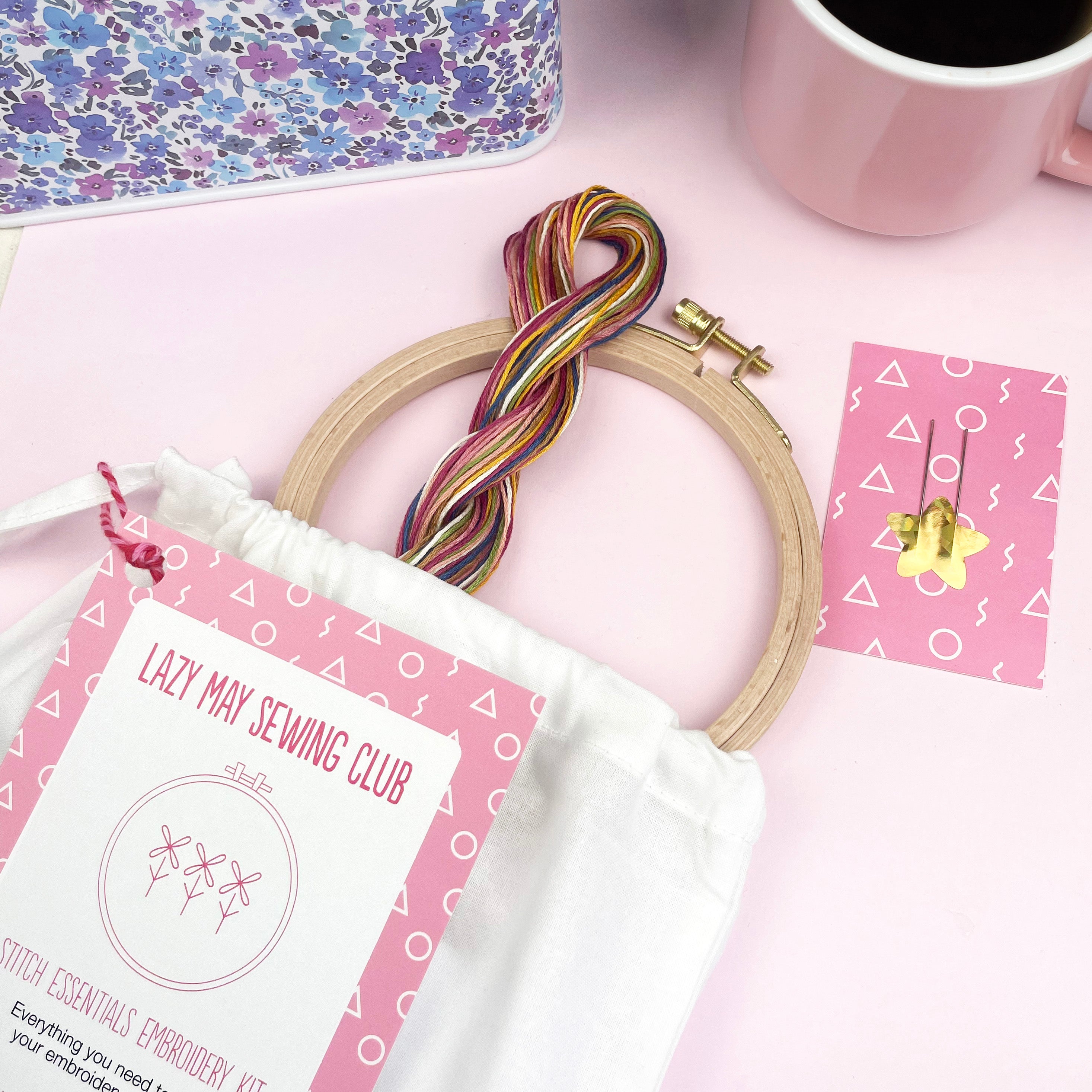 Embroidery hoop with multicolored threads, needle, and a beginner-friendly embroidery kit pouch on a pink surface
