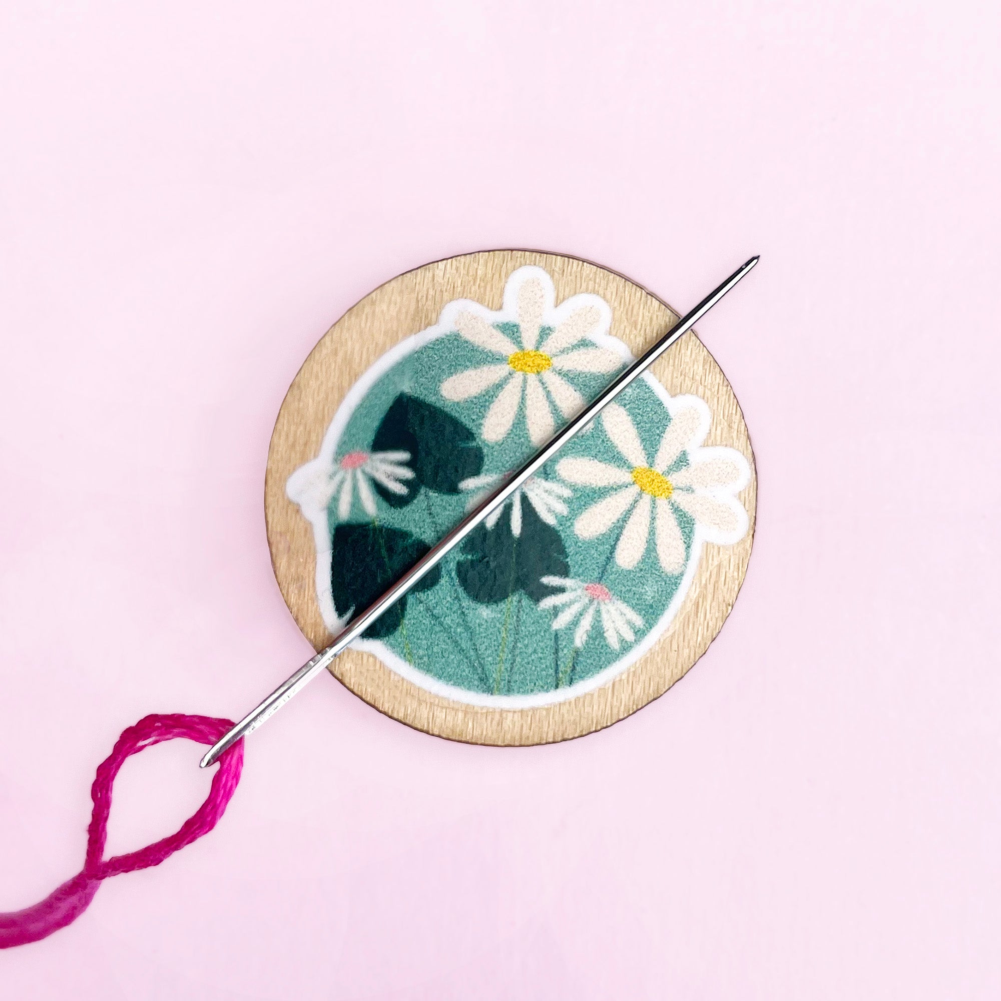 Embroidery needle minder with floral design and needle on a pink background