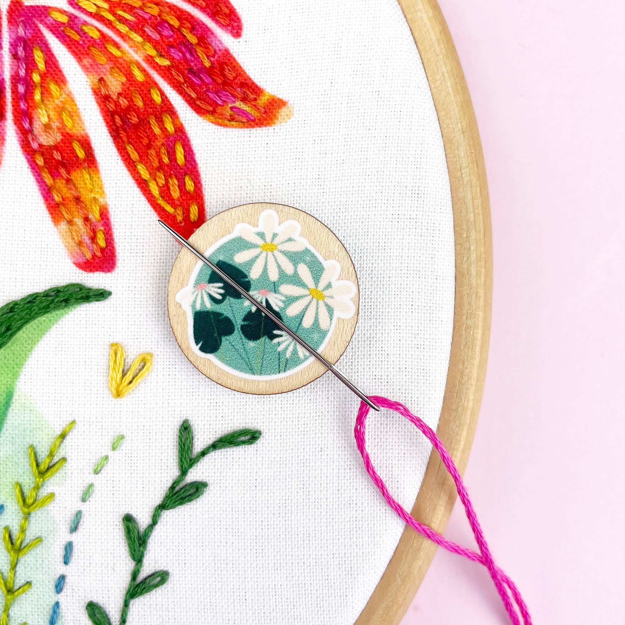 Embroidery hoop with floral embroidery and a wooden needle minder with floral design.