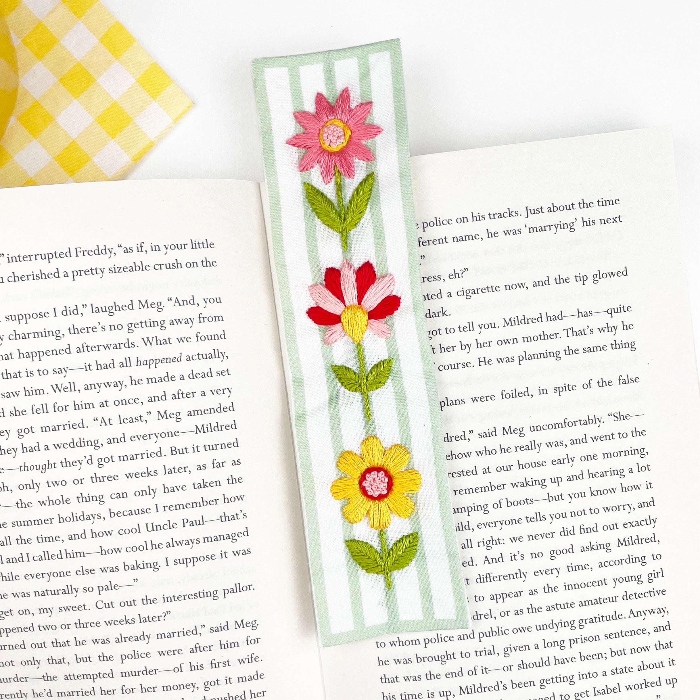 Floral bookmark on a book with a yellow checkered fabric background. DIY floral embroidery kit makes a perfect book lover gift or creative reading accessory.