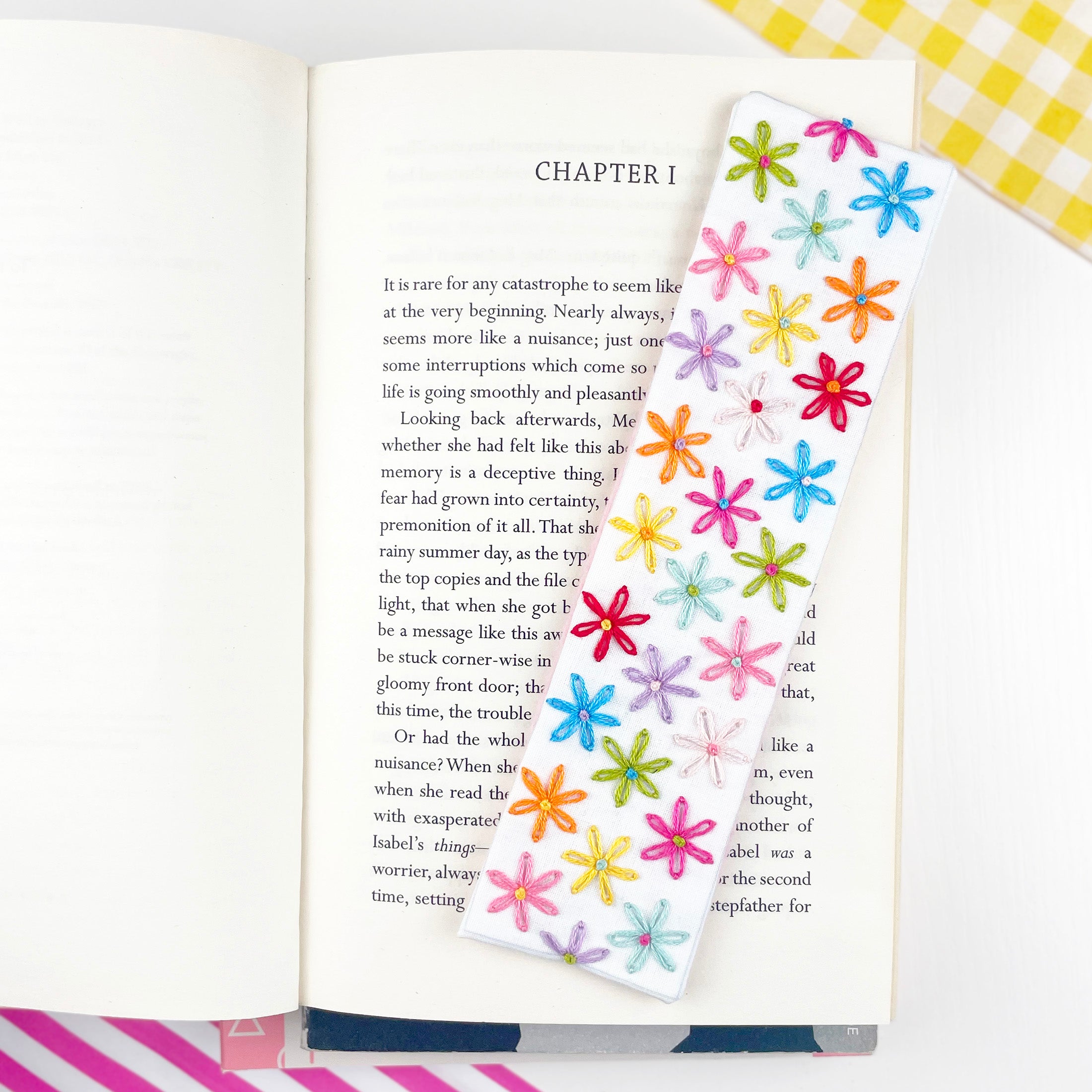 Open book with colorful flower-shaped bookmarks on a checkered background.  Hand embroidered bookmark making kit