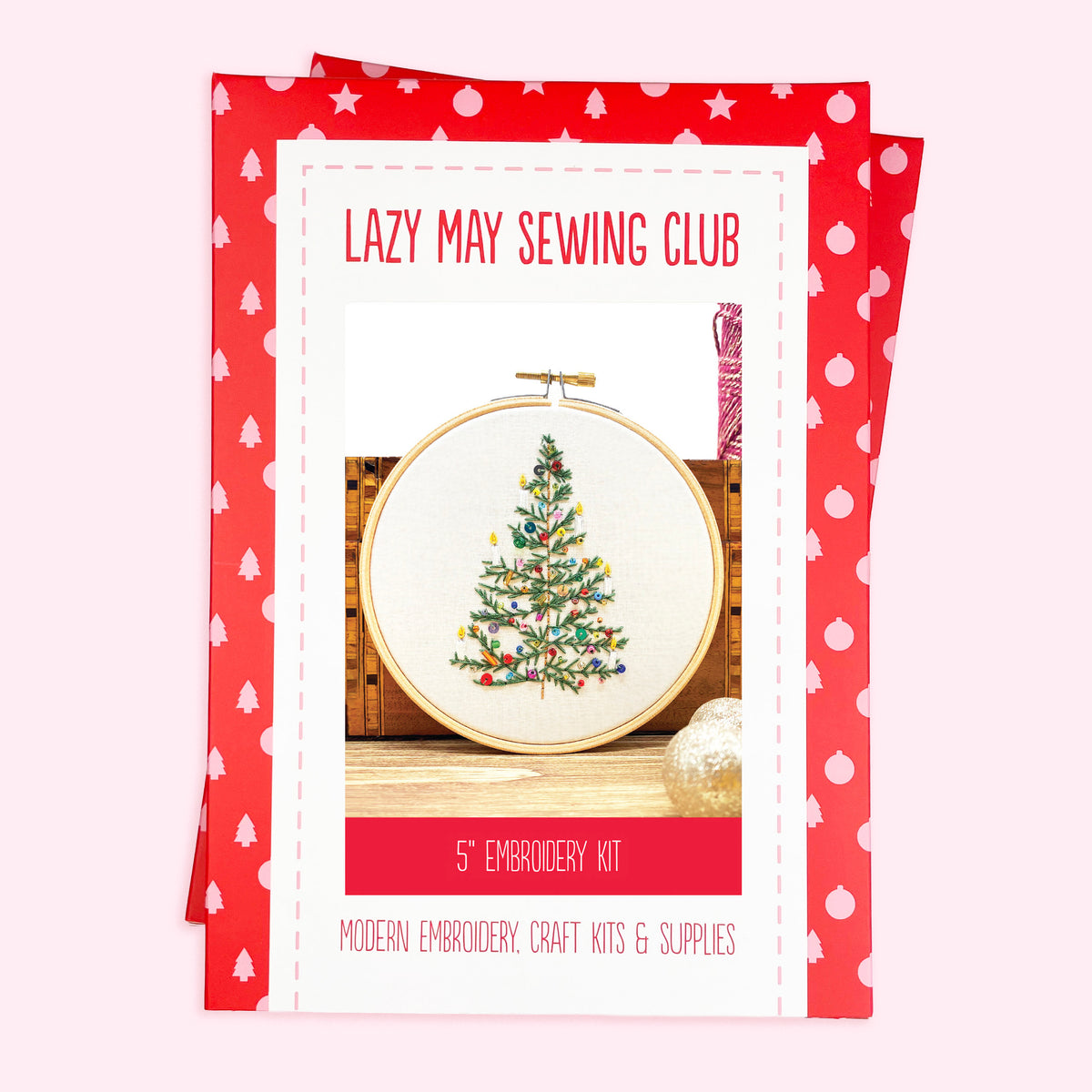 A Christmas-themed embroidery kit package from Lazy May Sewing Club, featuring a red and white patterned border and a central photo of a completed embroidered Christmas tree in an embroidery hoop.