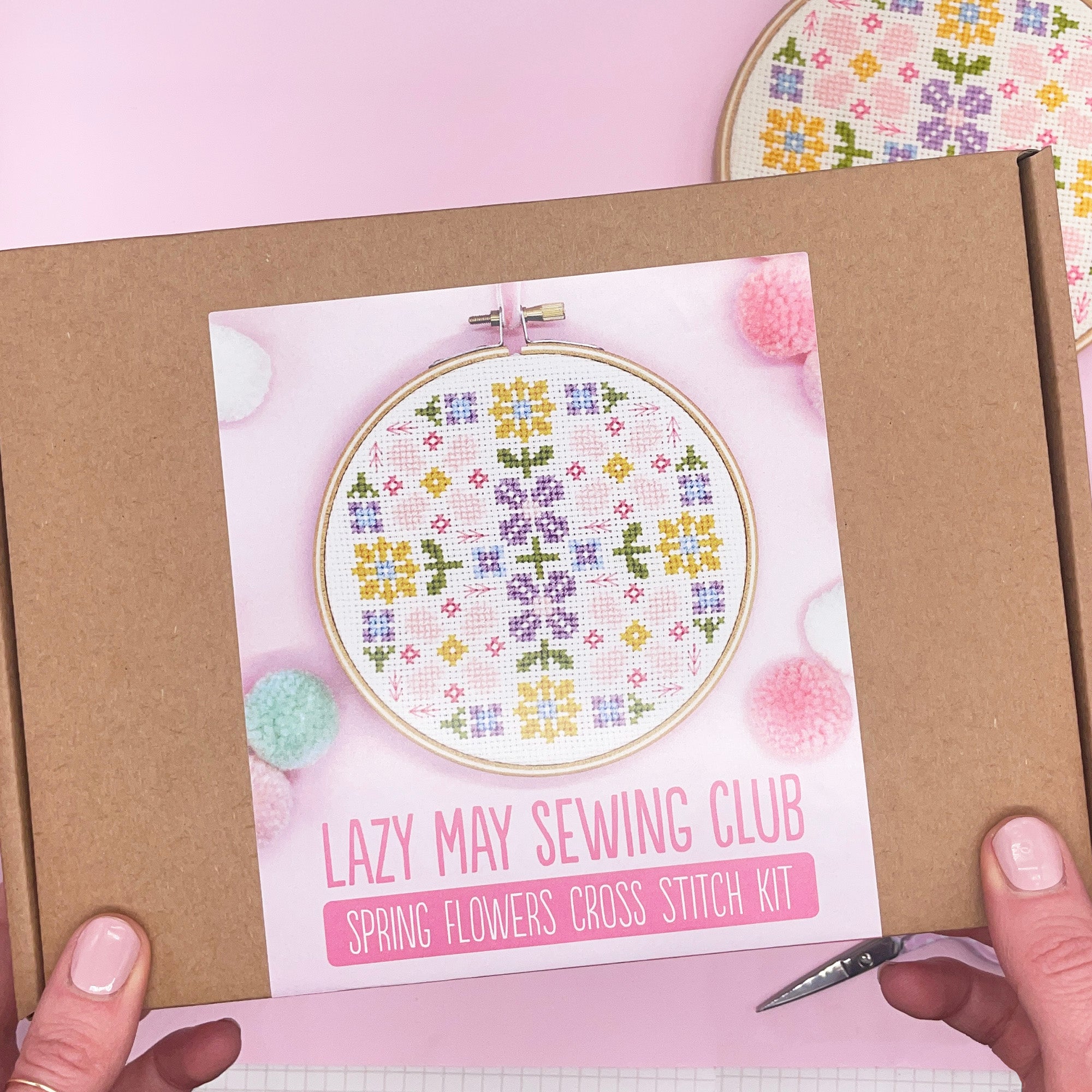 The cross-stitch kit packaged in a craft box, with all materials securely placed inside. The box is adorned with a label featuring the floral design, making it suitable for gifting.