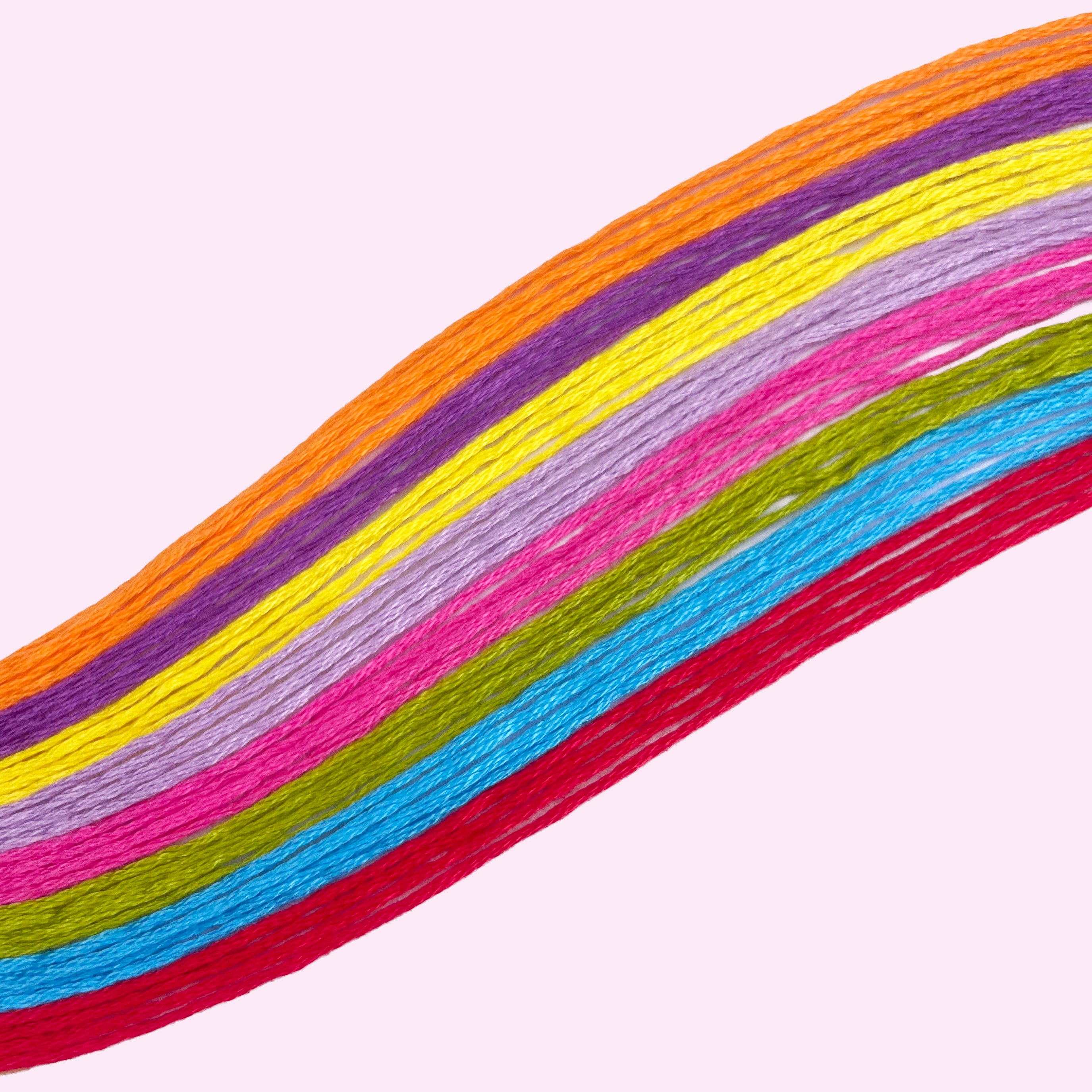 Brightly colored embroidery threads laid out in a curved arrangement on a light pink background