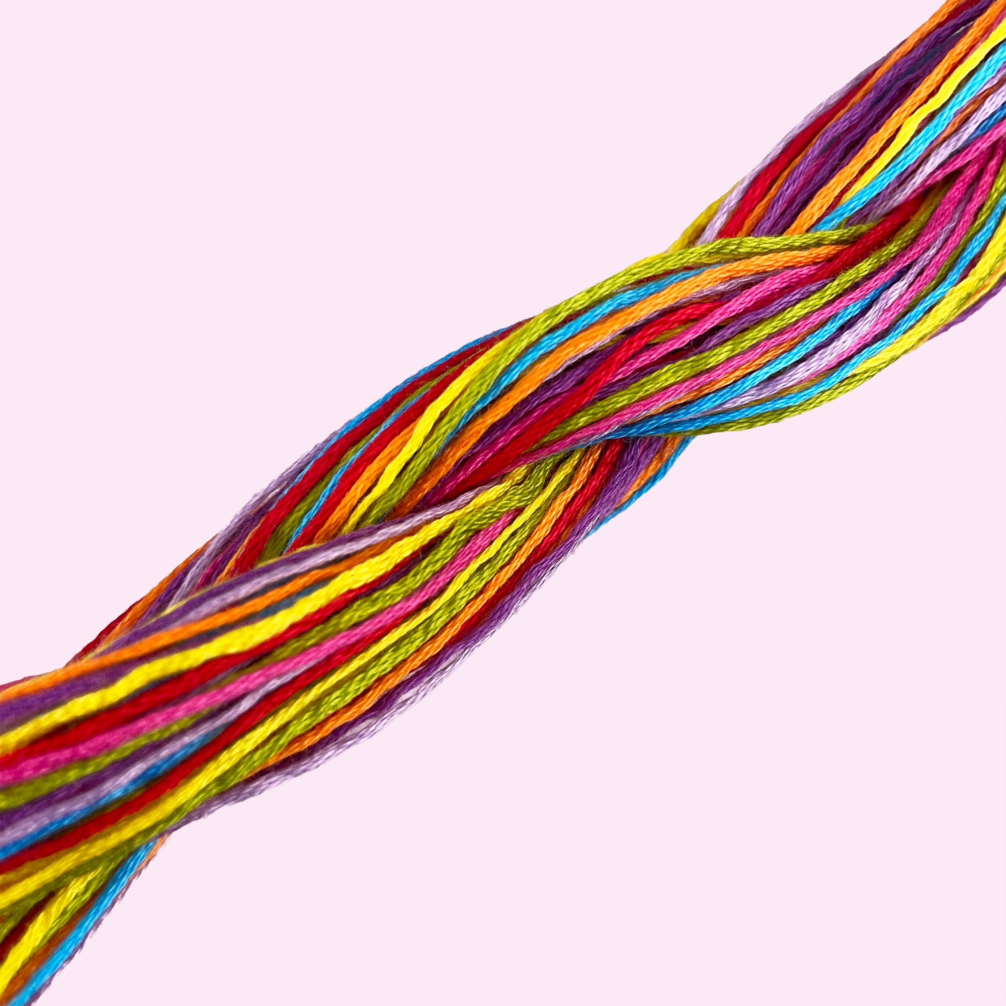 Brightly colored embroidery threads twisted together against a soft pink background for beginner kits.